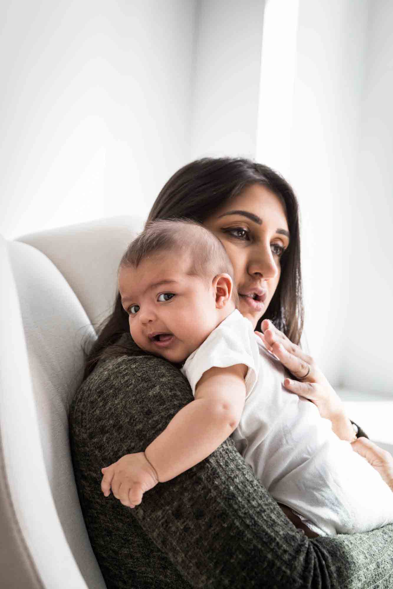 Mother sitting in chair holding baby by window during a NYC family portrait session