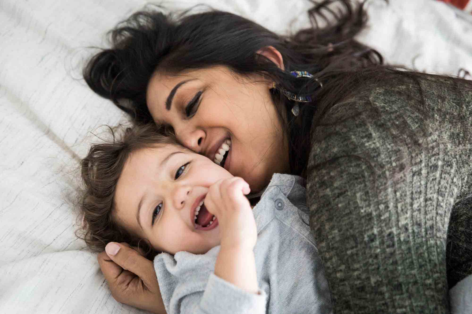 Laughing mother kissing toddler on the bed during a NYC family portrait session