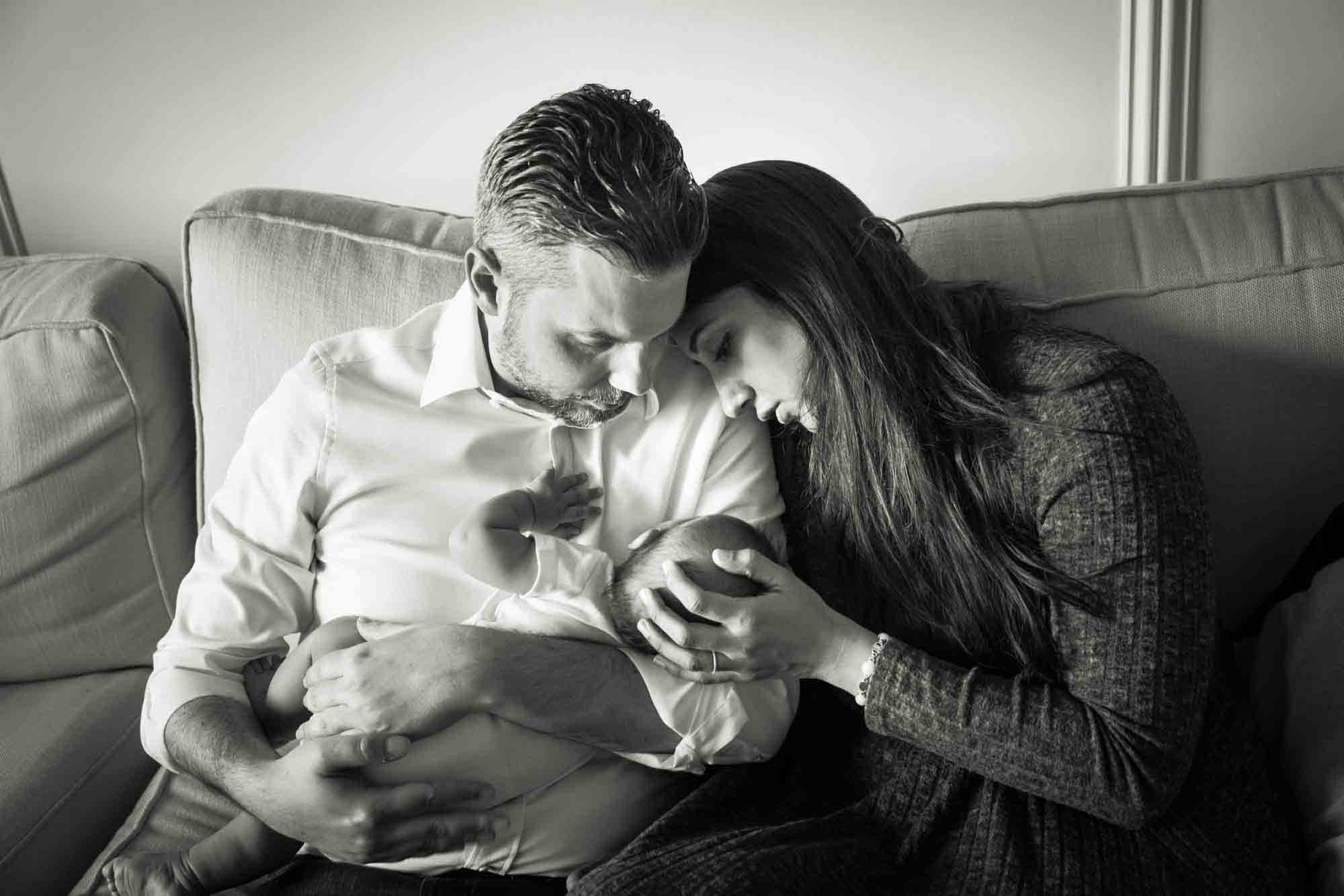 Black and white photo of parents looking at newborn while sitting on couch