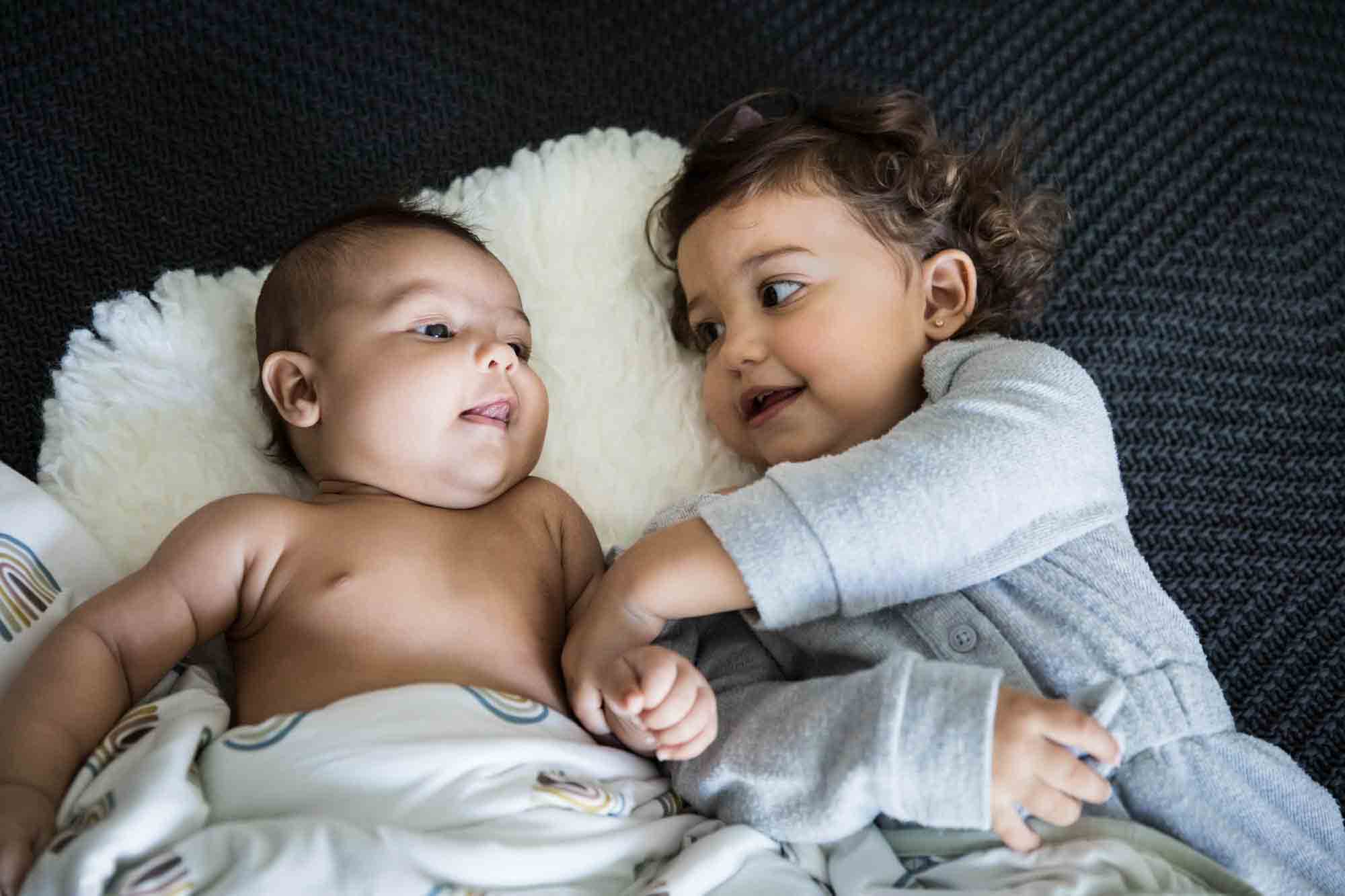 Toddler holding hand of baby on white rug during a Manhattan family portrait session