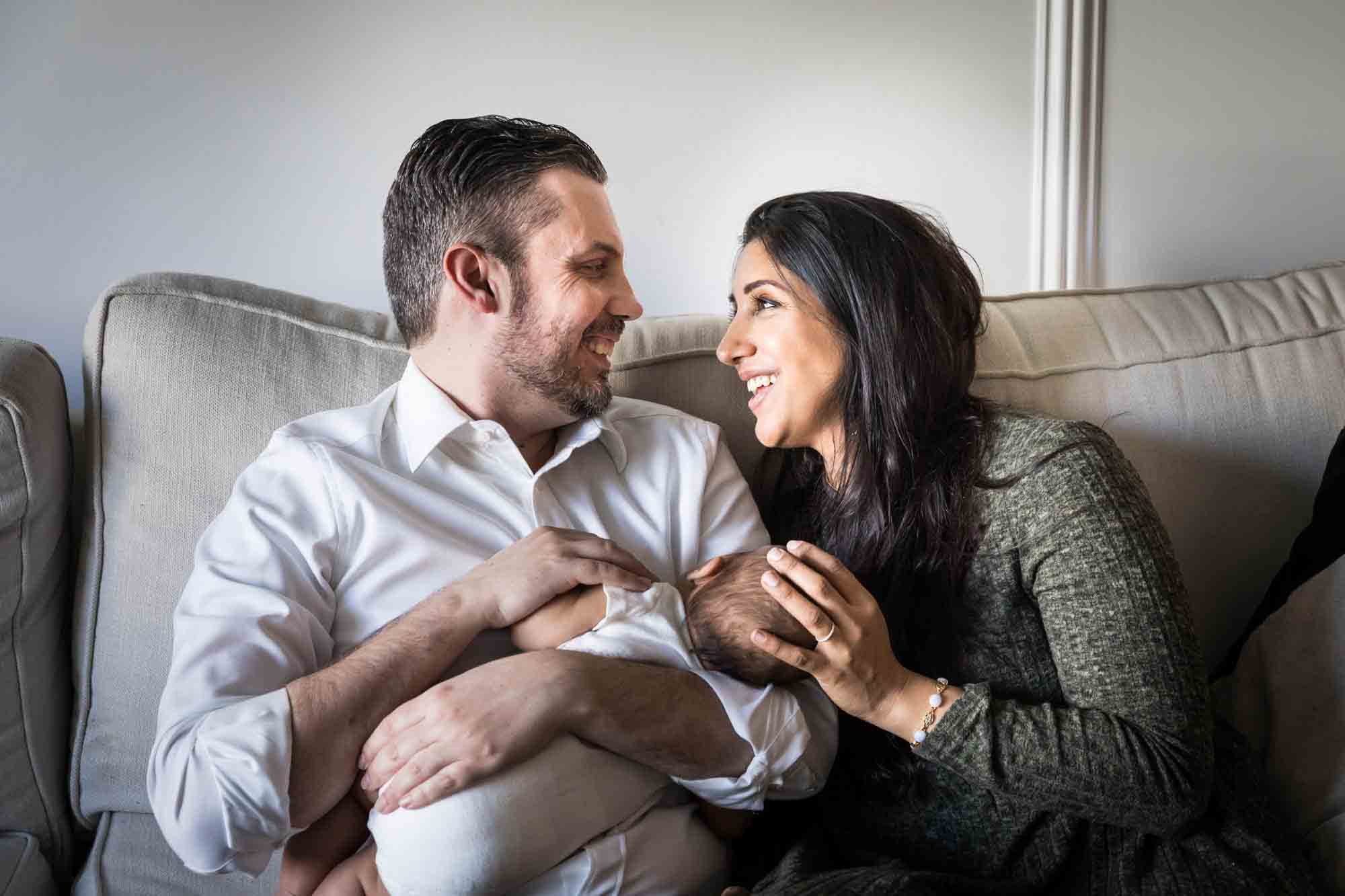 Manhattan family portrait session of parents holding baby on couch looking at each other