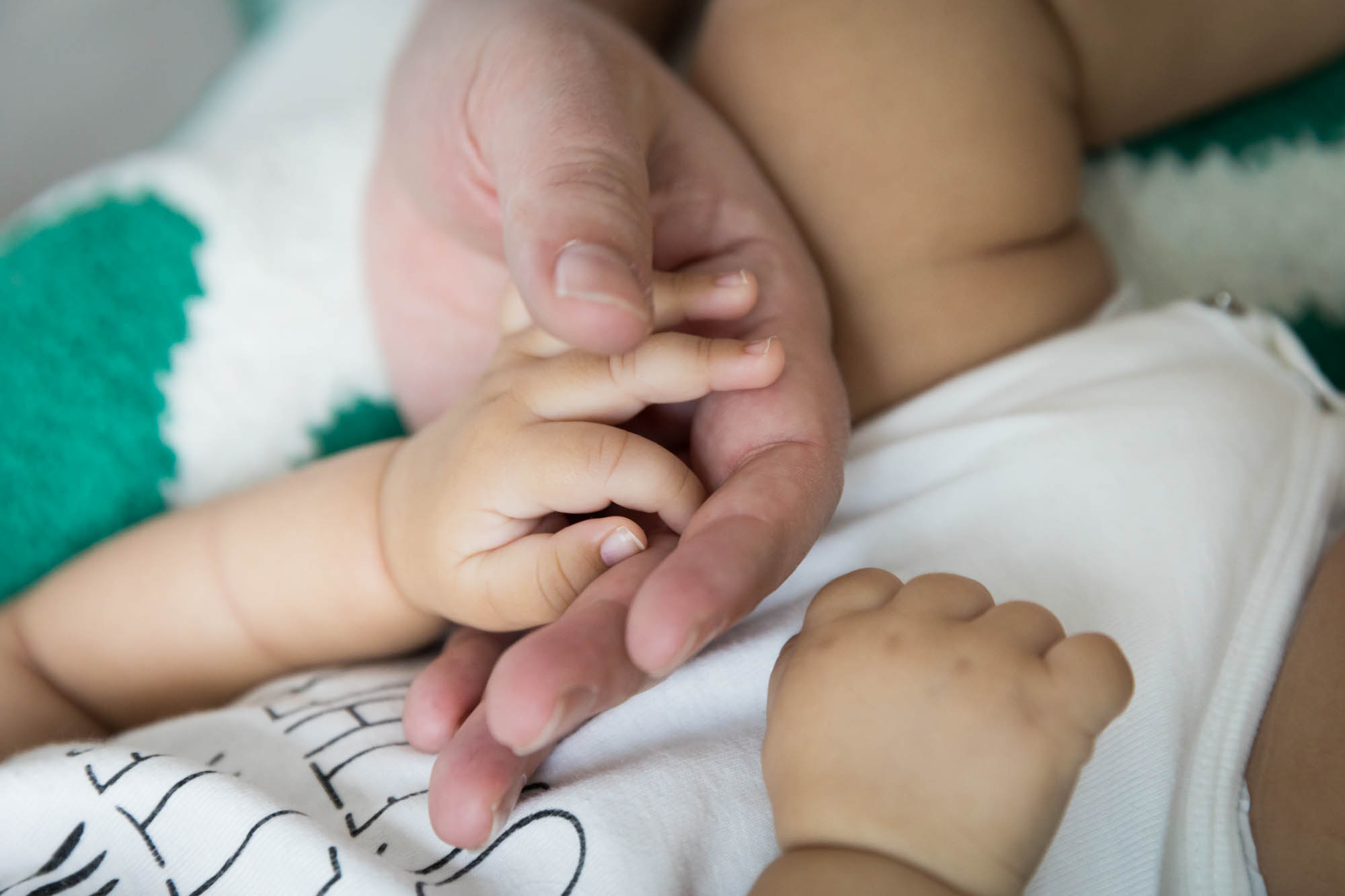 Father's hand holding newborn baby hand on green and white blanket during a New York family portrait session