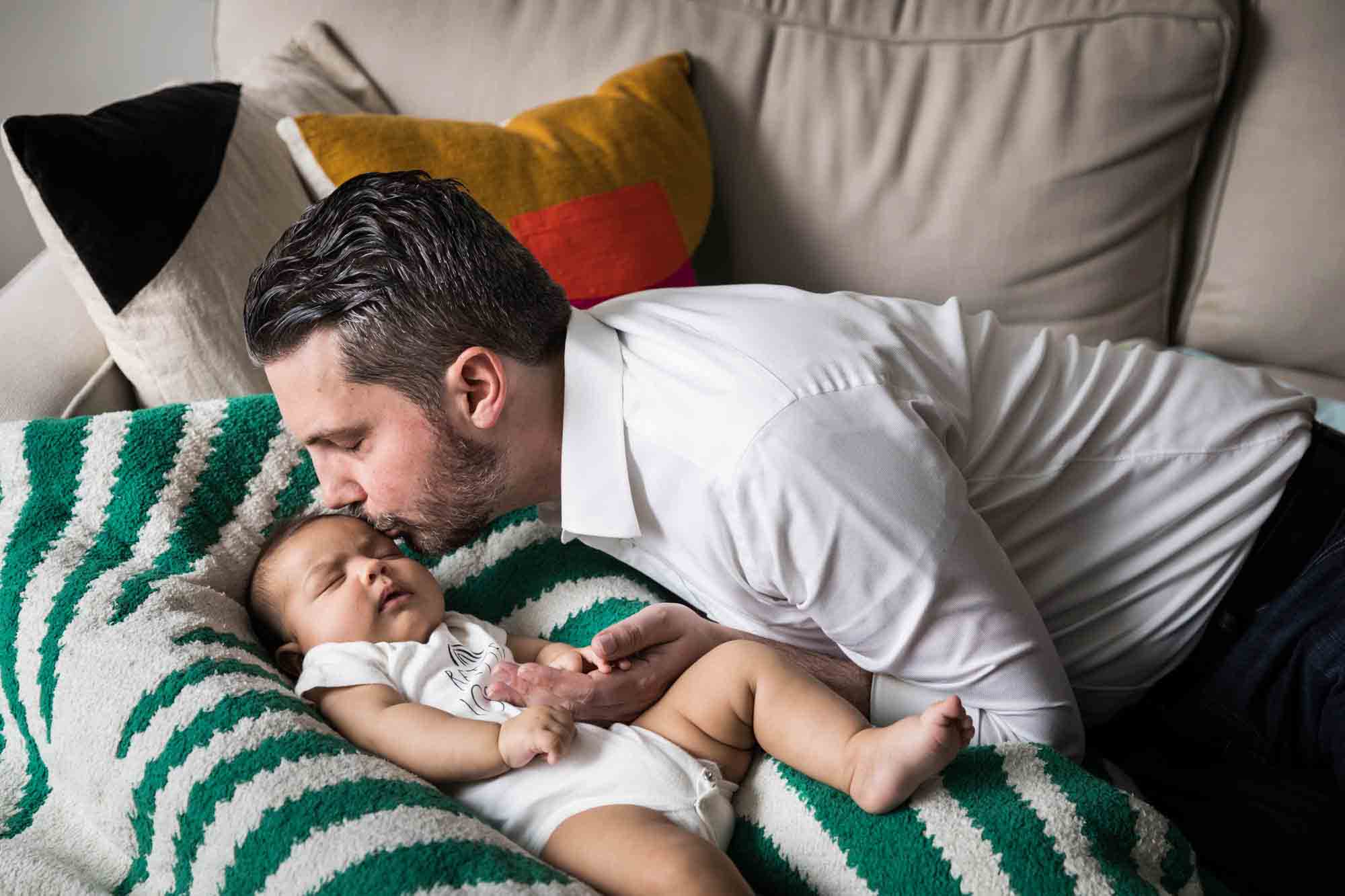 Father kissing newborn baby on green and white blanket on couch