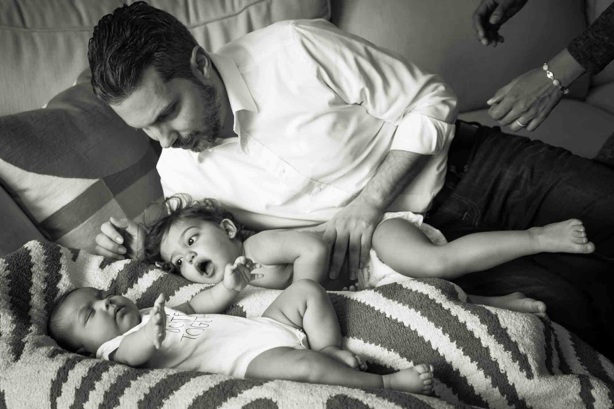 Black and white photo of father playing with baby and toddler on couch