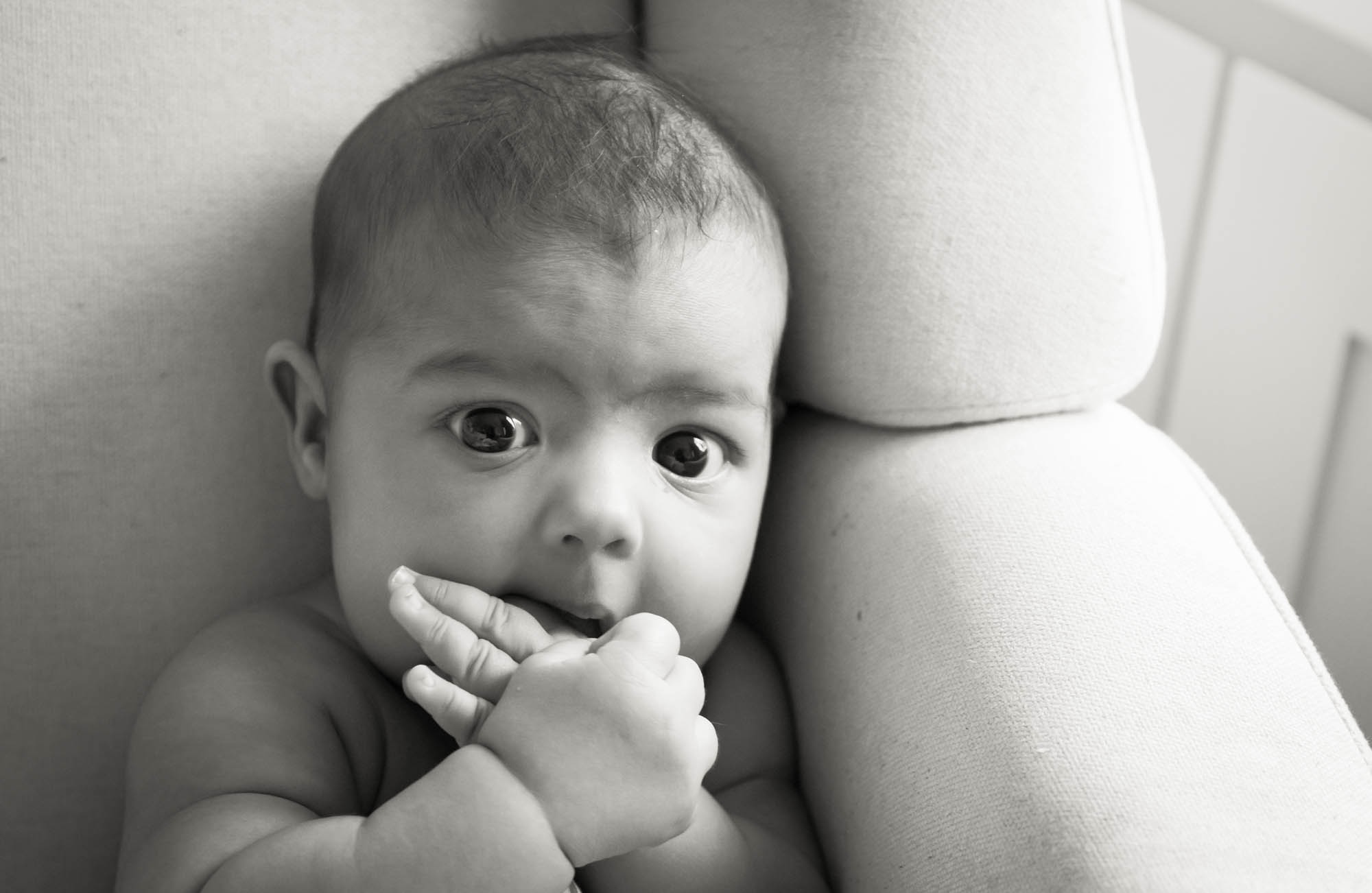 Black and white photo of baby with hands in mouth sitting in chair