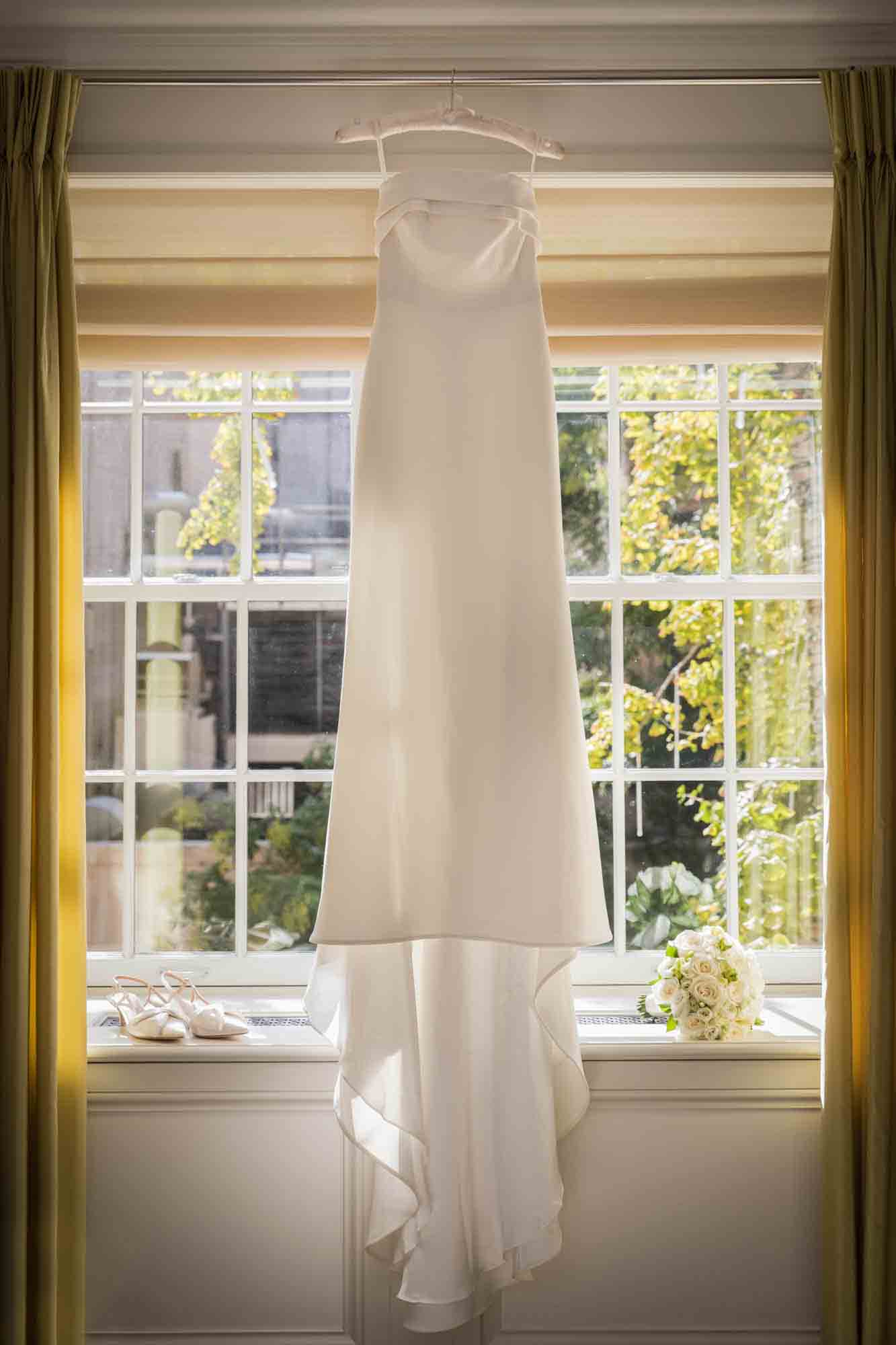 Wedding dress, white high heels, and flower bouquet in front of window in Mark Hotel
