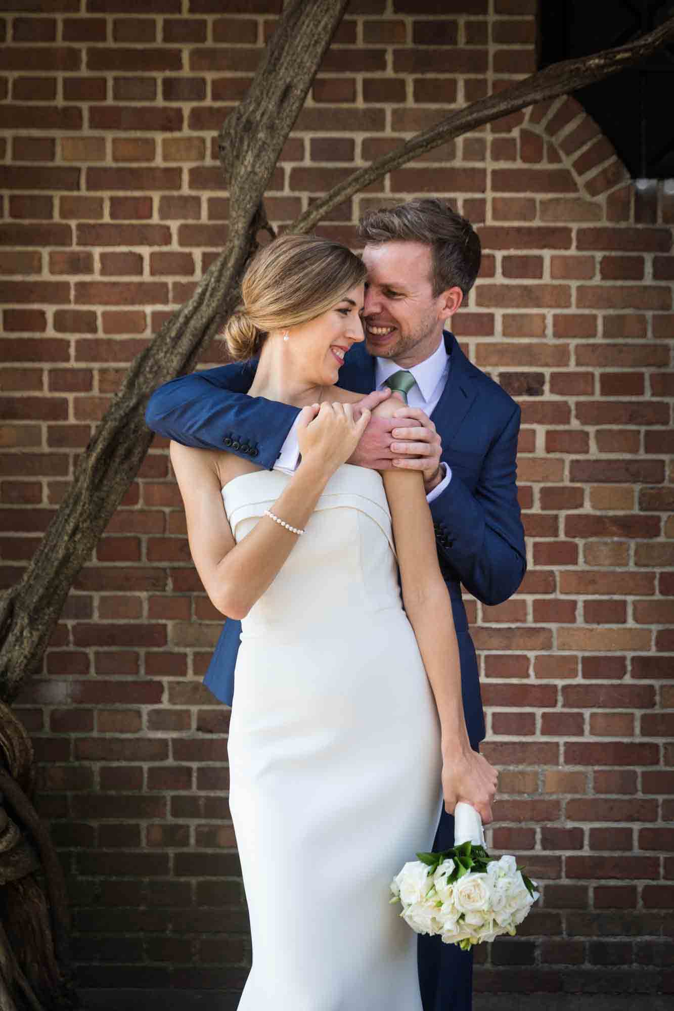 Couple hugging in front of brick wall during a Conservatory Garden wedding in Central Park