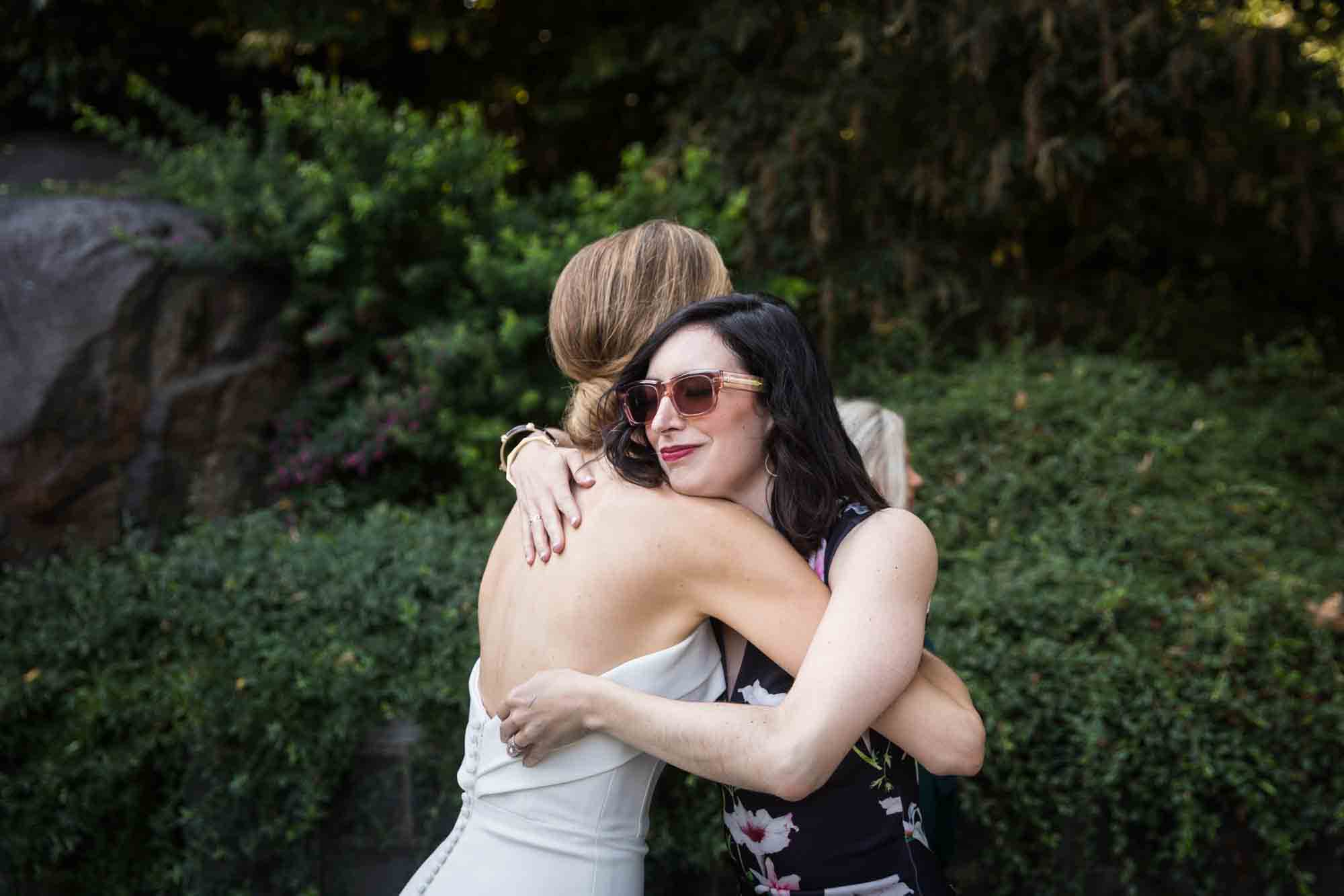 Bride hugging female guest wearing sunglasses during a Conservatory Garden wedding in Central Park