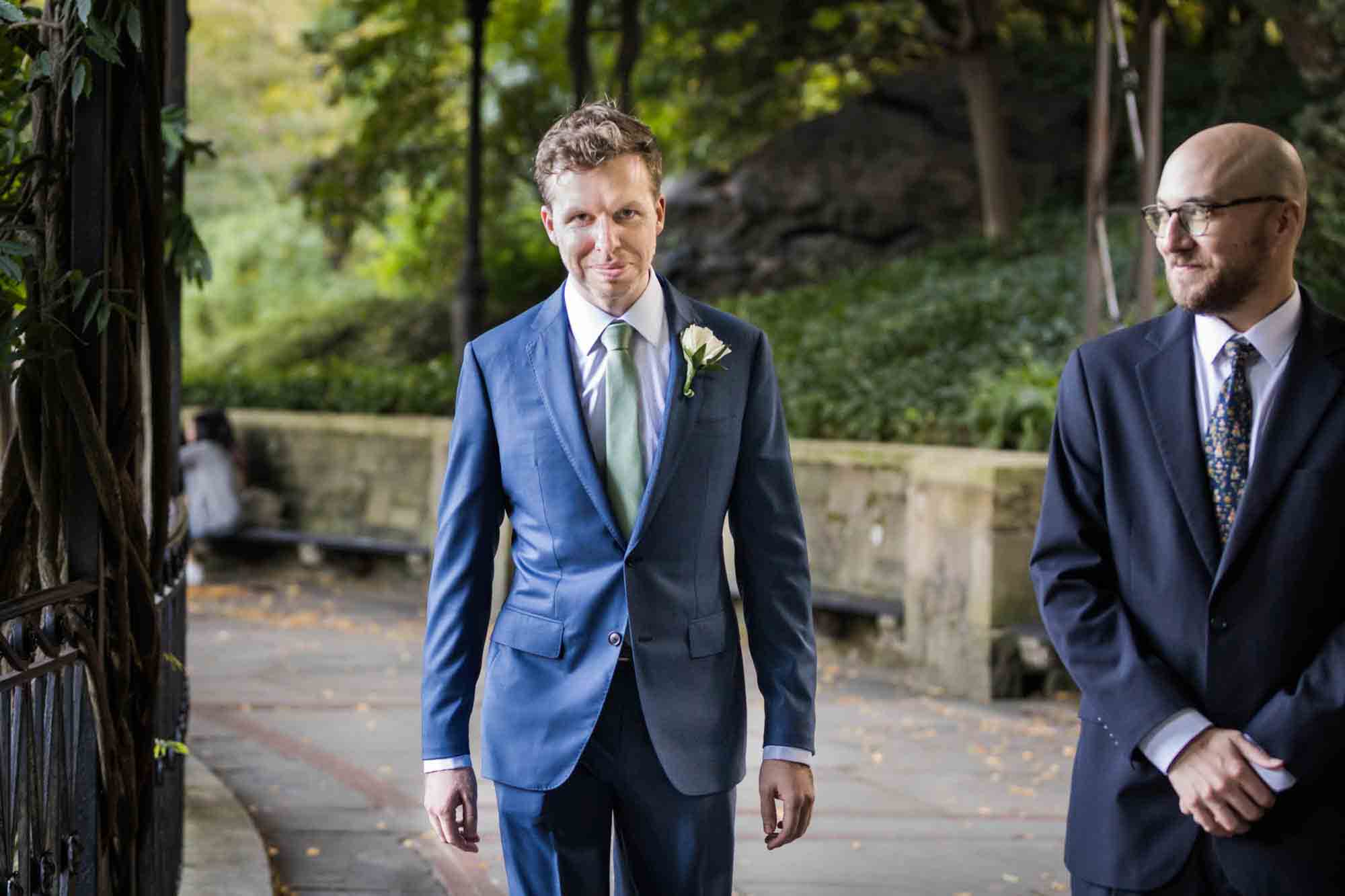Groom wearing blue suit walking up aisle on Wisteria Terrace during a Conservatory Garden wedding in Central Park