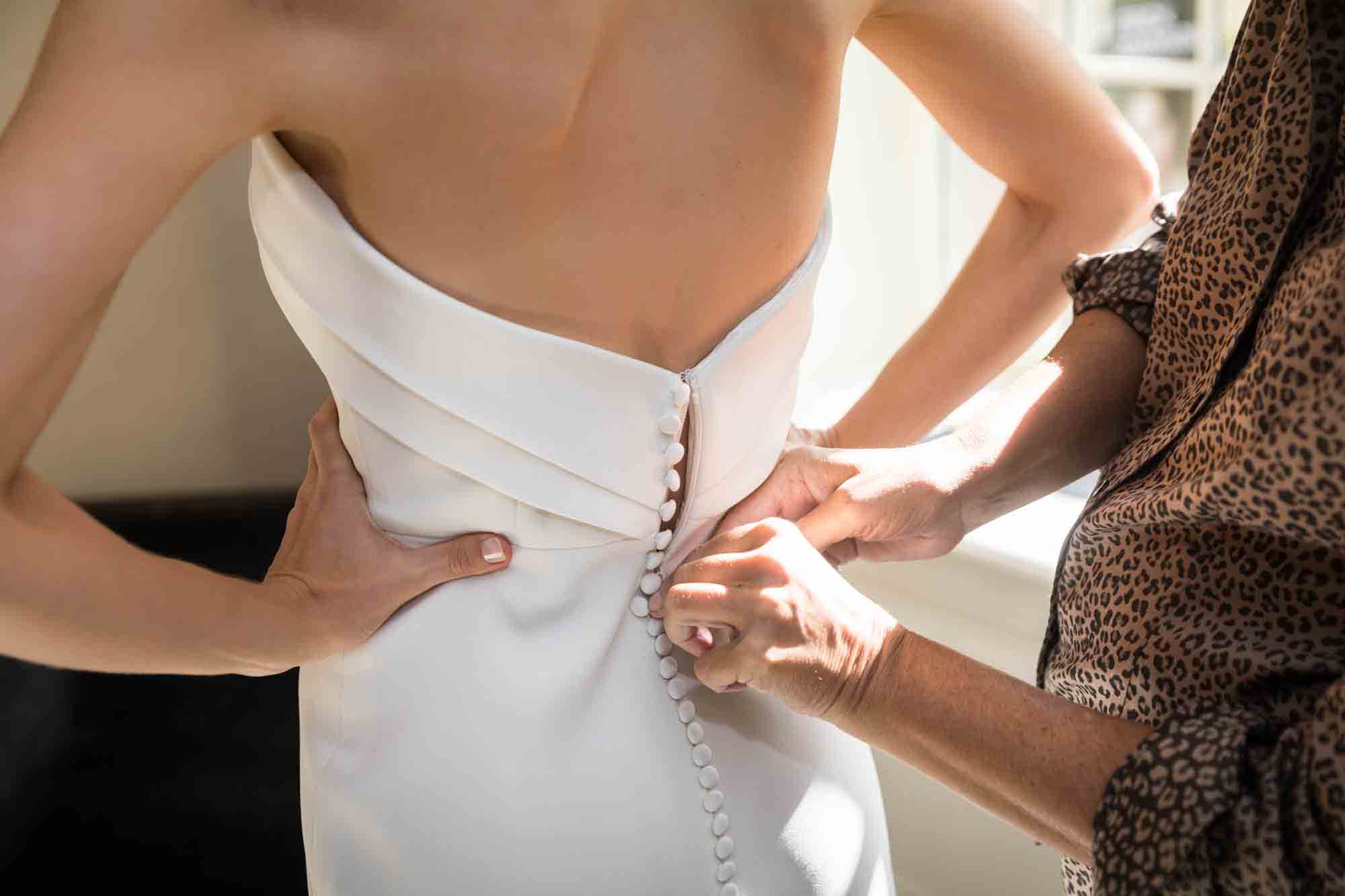 Close up of mother's hands zipping up bride's wedding dress