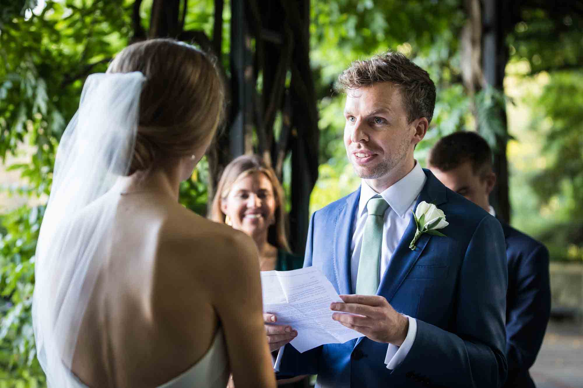 Groom holding paper and saying vows to bride during a Conservatory Garden wedding in Central Park