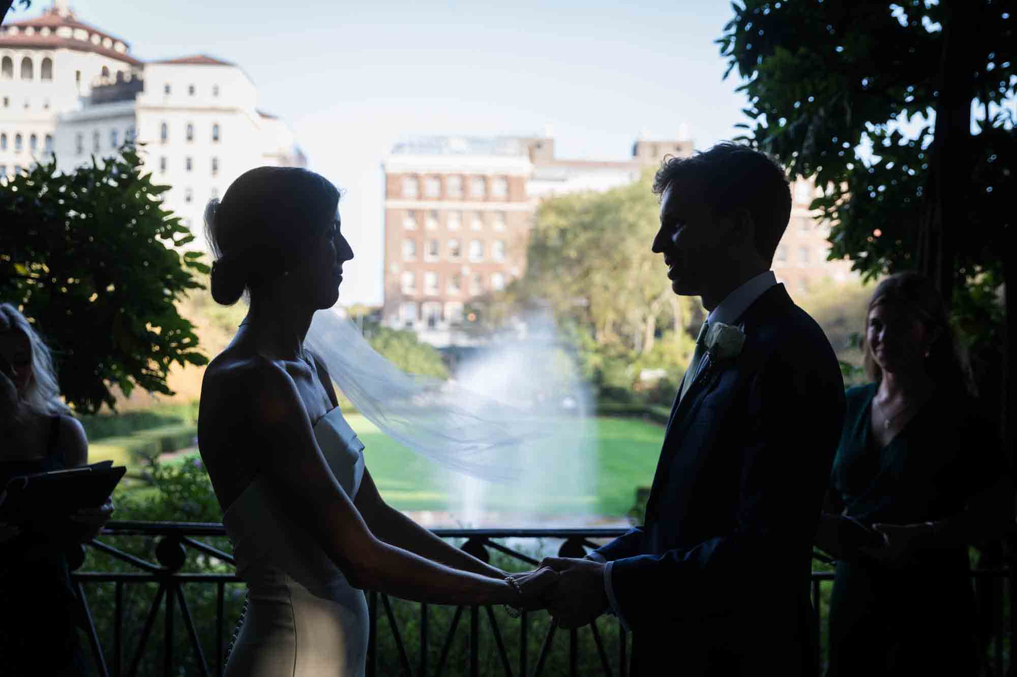 Backlit photo of bride and groom holding hands in front of fountain during a Conservatory Garden wedding in Central Park