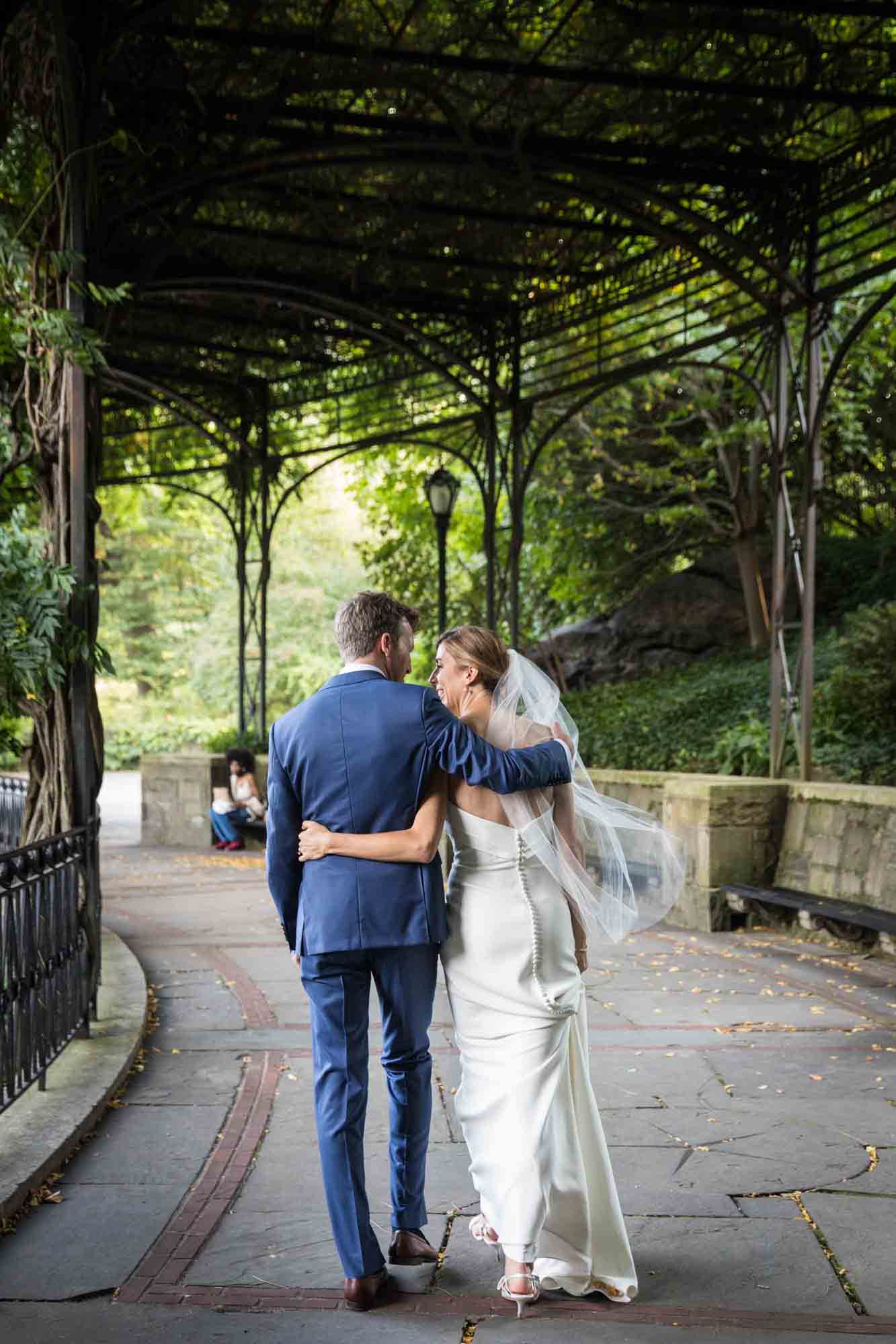 Bride and groom walking on Wisteria Terrace with arms around each other during a Conservatory Garden wedding in Central Park