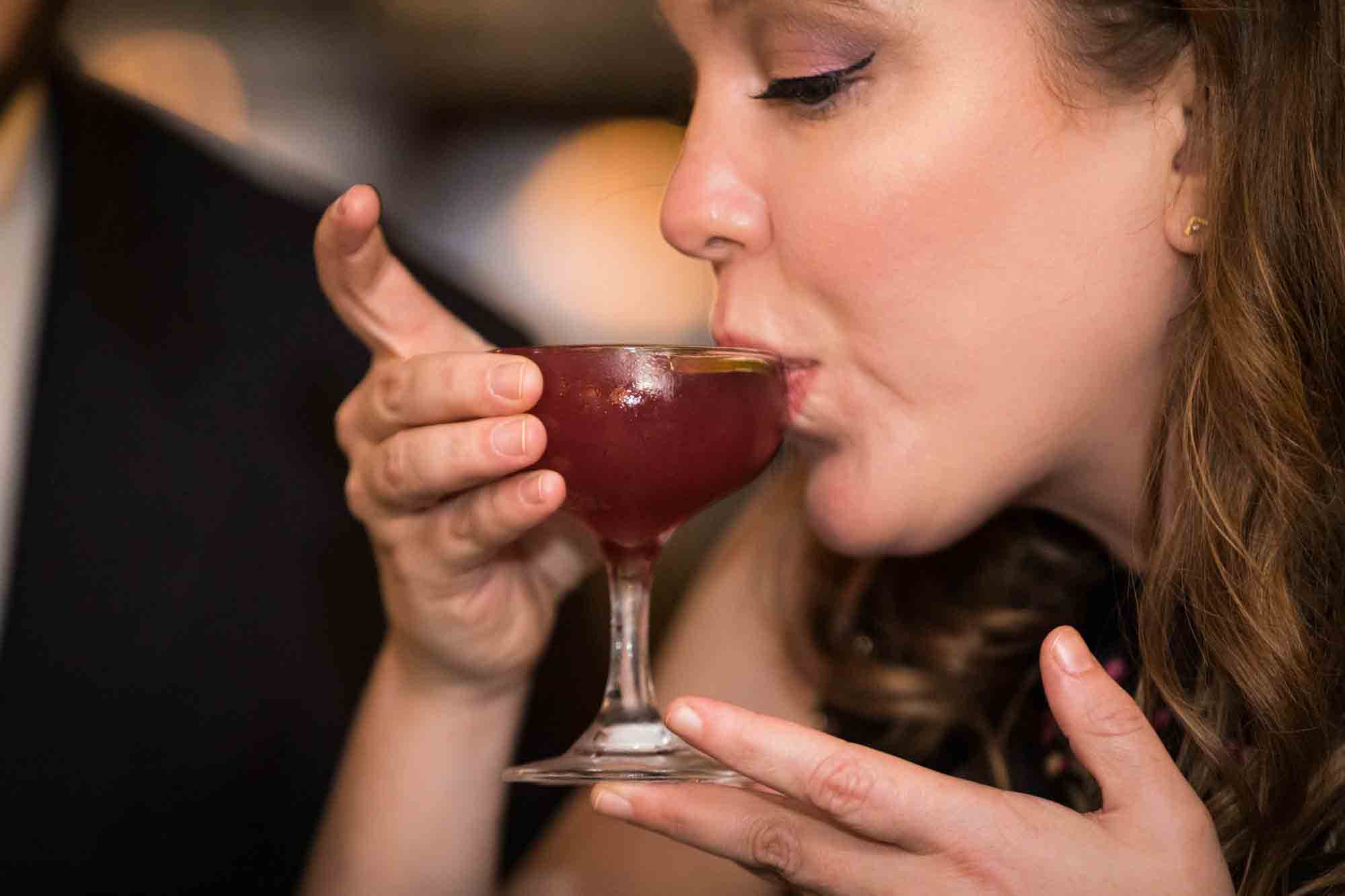 Woman sipping red colored drink from old fashioned champagne glass