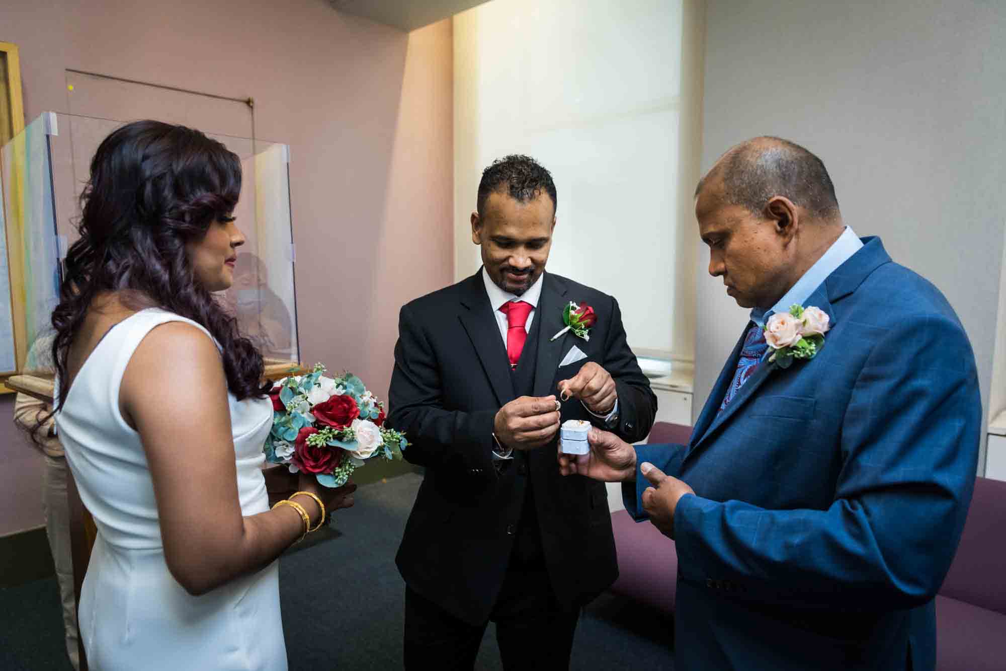 Groom selecting rings out of box in front of bride and older man  at a NYC City Hall wedding