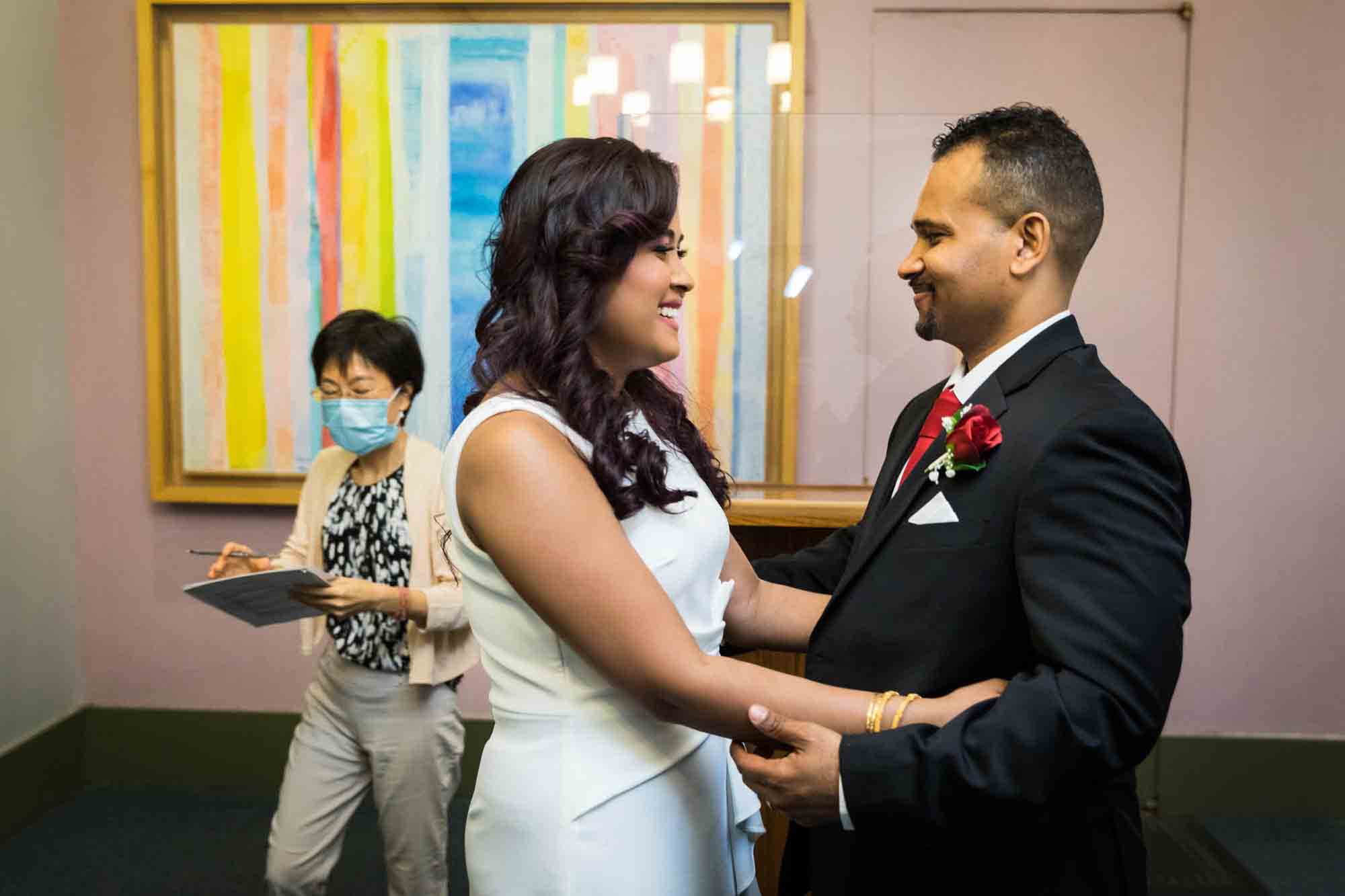 Bride and groom hugging in front of officiant and colorful striped painting for an article on how to elope in NYC
