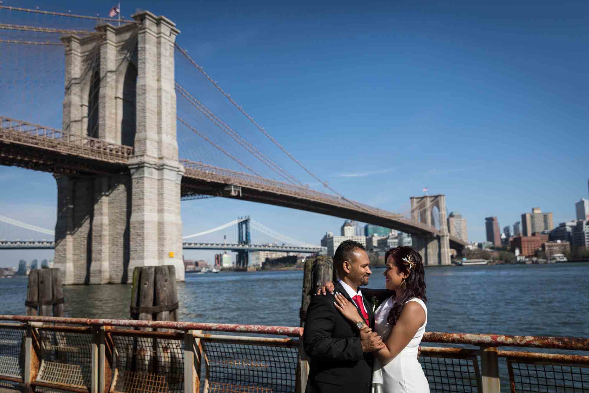 Bride and groom dancing on sidewalk in front of Brooklyn Bridge