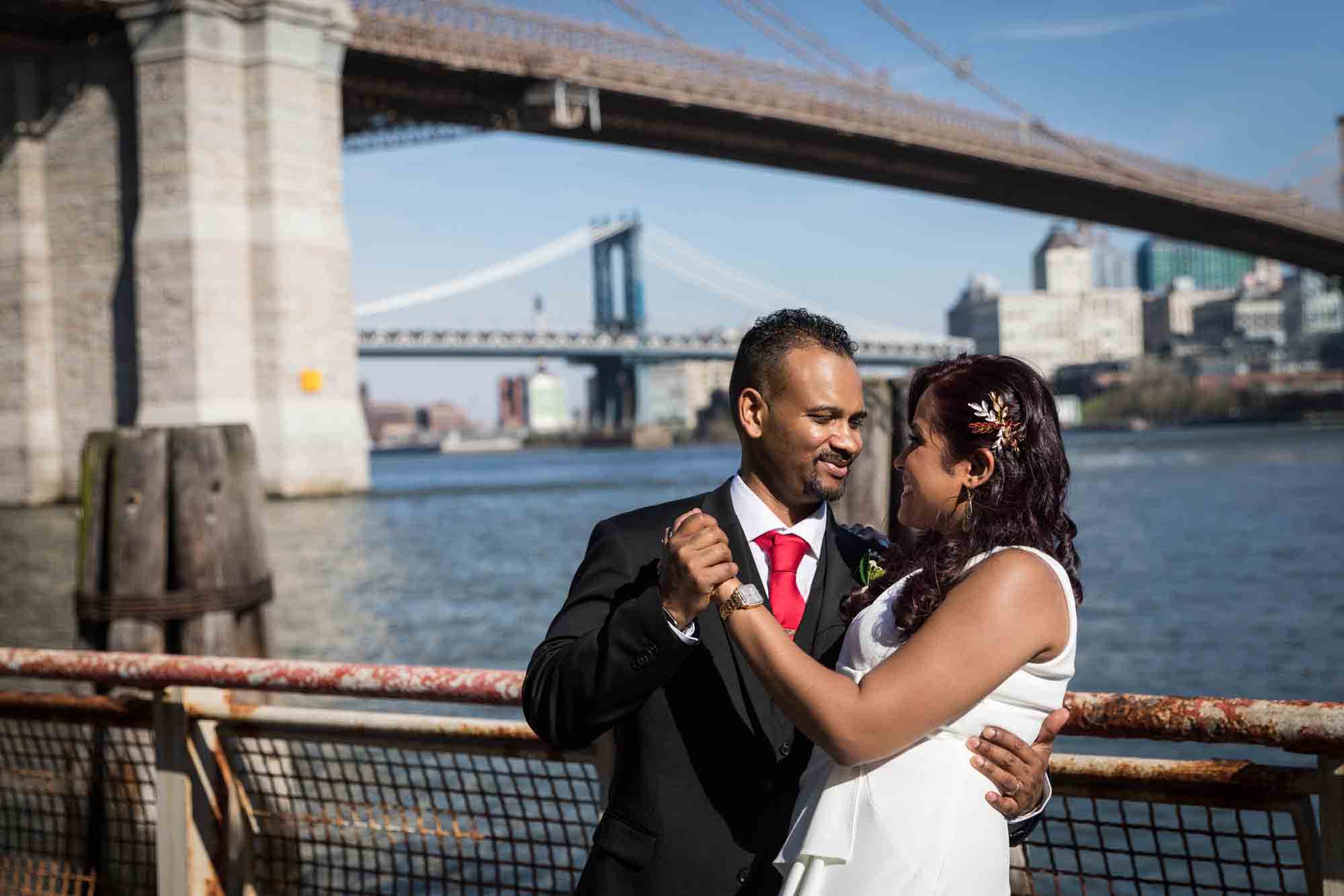 Bride and groom dancing in front of railing and Brooklyn Bridge