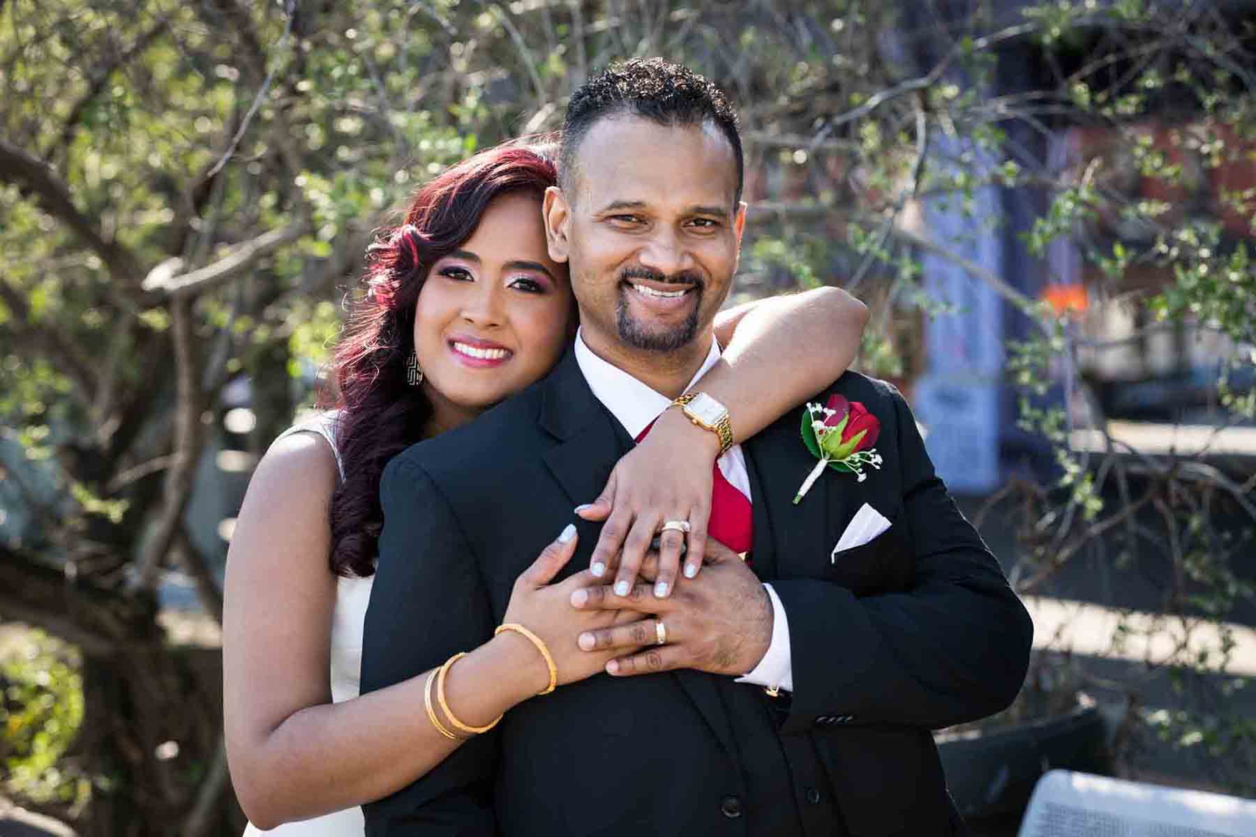 Bride with arms hugging groom and hands showing wedding rings