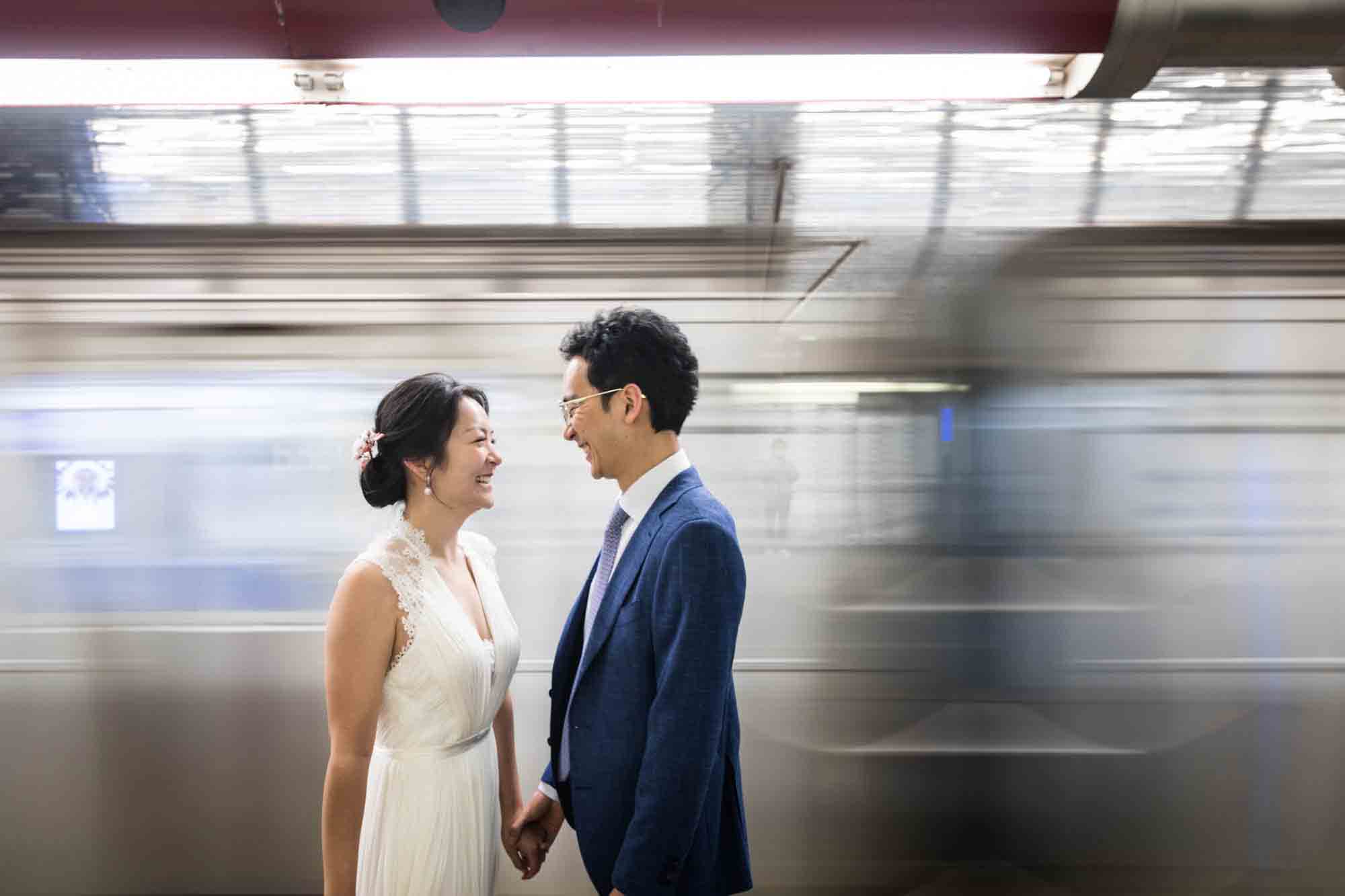 Couple standing in front of blurry subway train during a Roosevelt Island engagement photo shoot