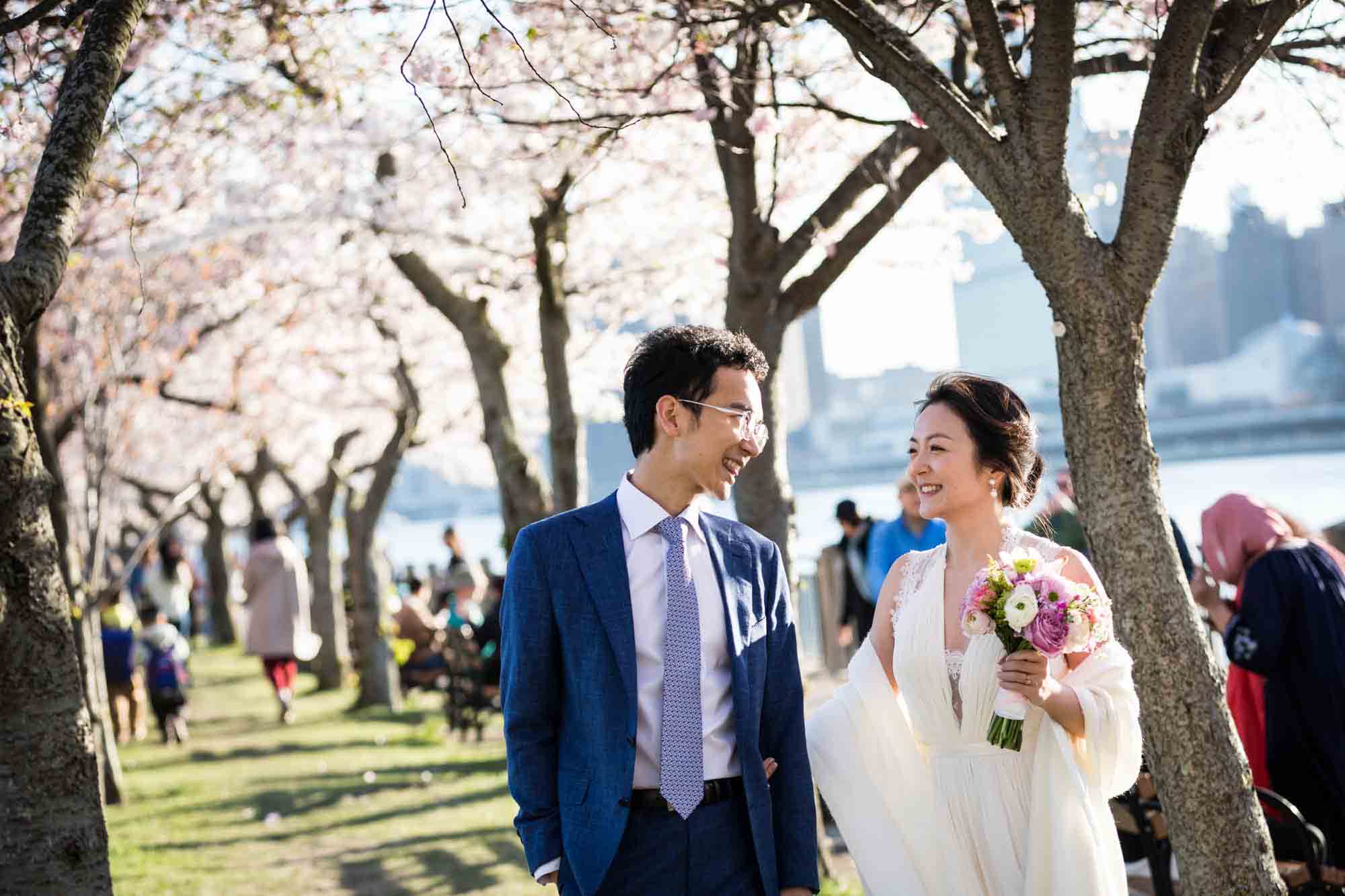 Couple walking under cherry blossom trees during a Roosevelt Island engagement photo shoot