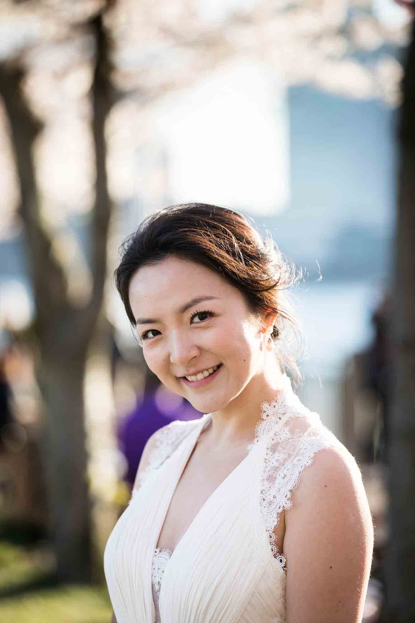 Woman wearing white sleeveless dress smiling into camera Couple walking under cherry blossom trees during a Roosevelt Island engagement photo shoot