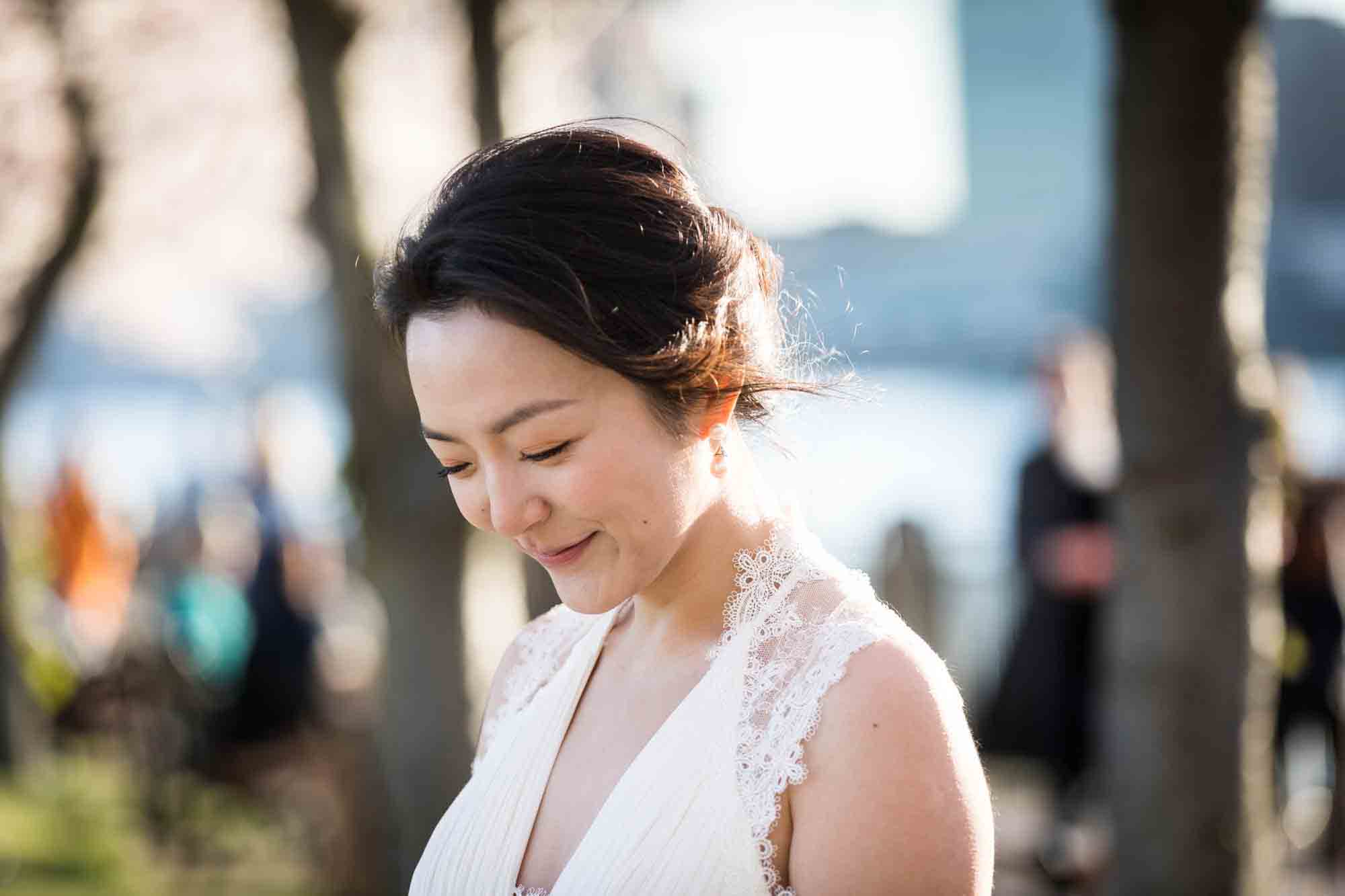 Woman wearing white dress looking down and smiling Couple walking under cherry blossom trees during a Roosevelt Island engagement photo shoot