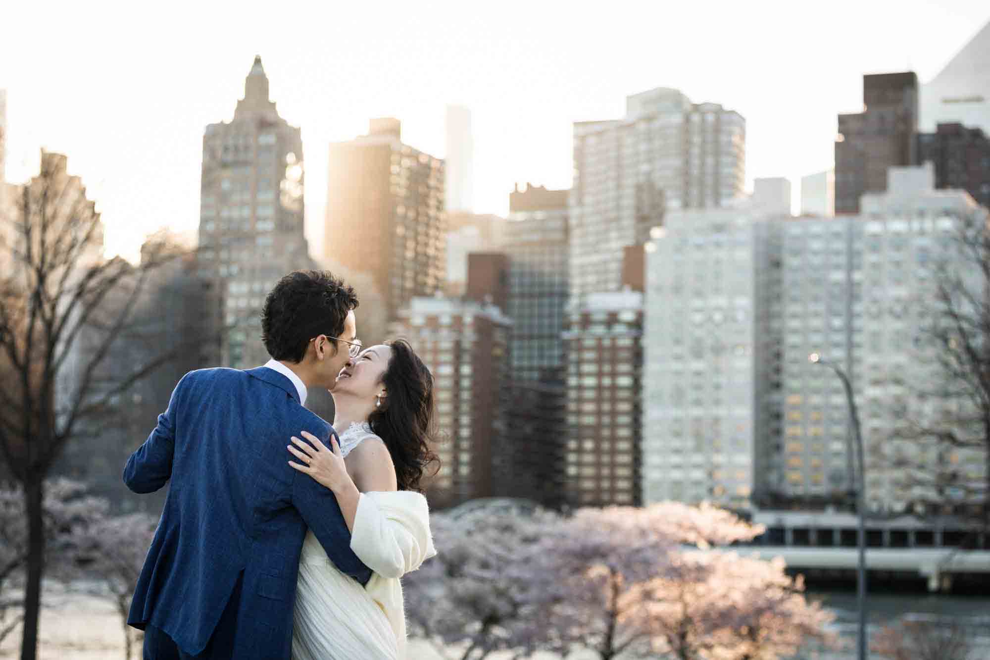 Couple kissing in front of NYC skyline at sunset during a Roosevelt Island engagement photo shoot