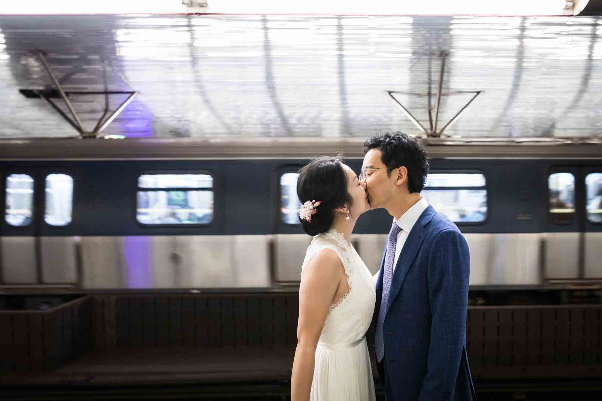 Couple kissing in subway station in front of moving train during a Roosevelt Island engagement photo shoot