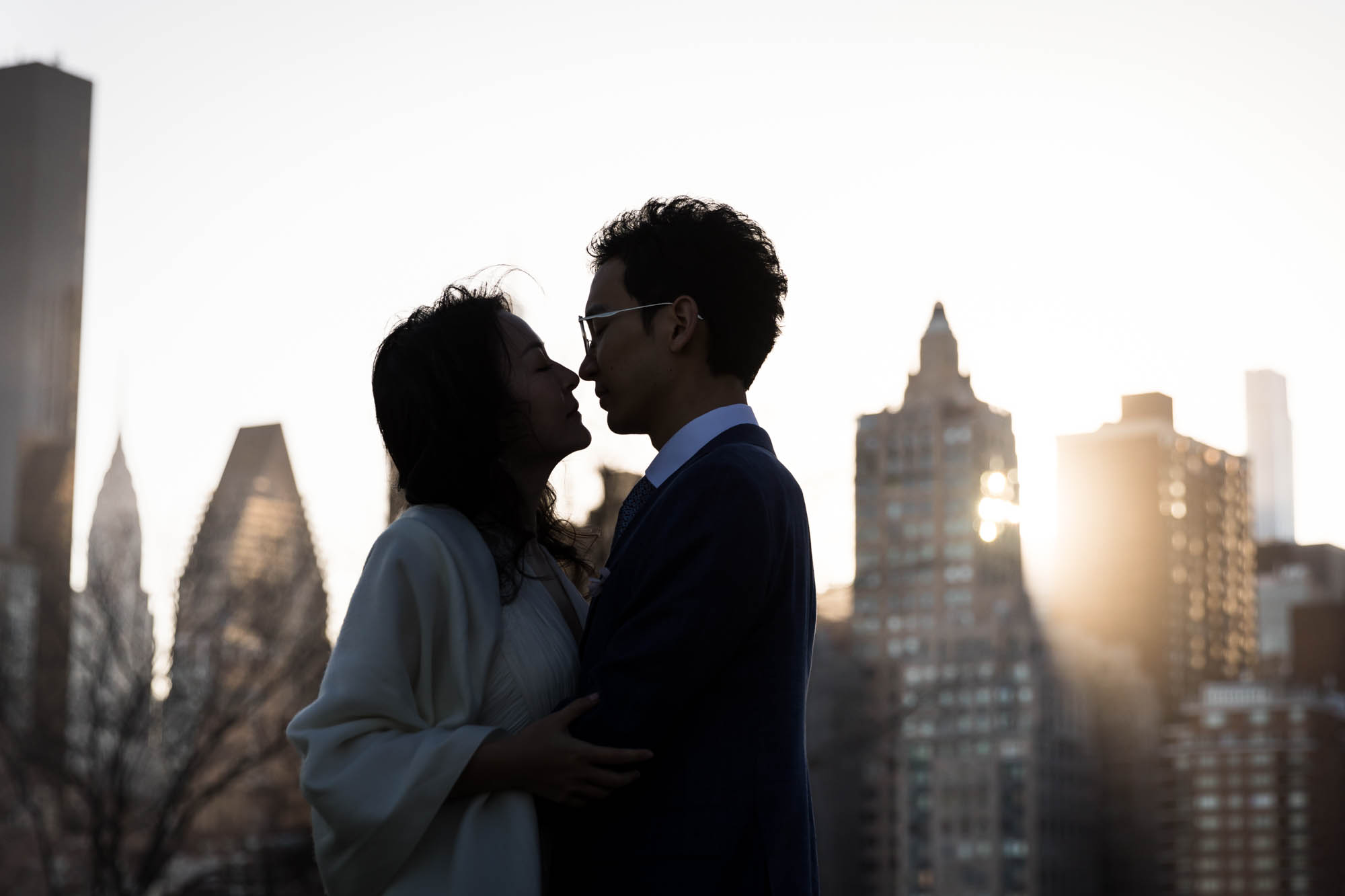 Roosevelt Island engagement photos of backlit photo of couple kissing in front of NYC skyline at sunset