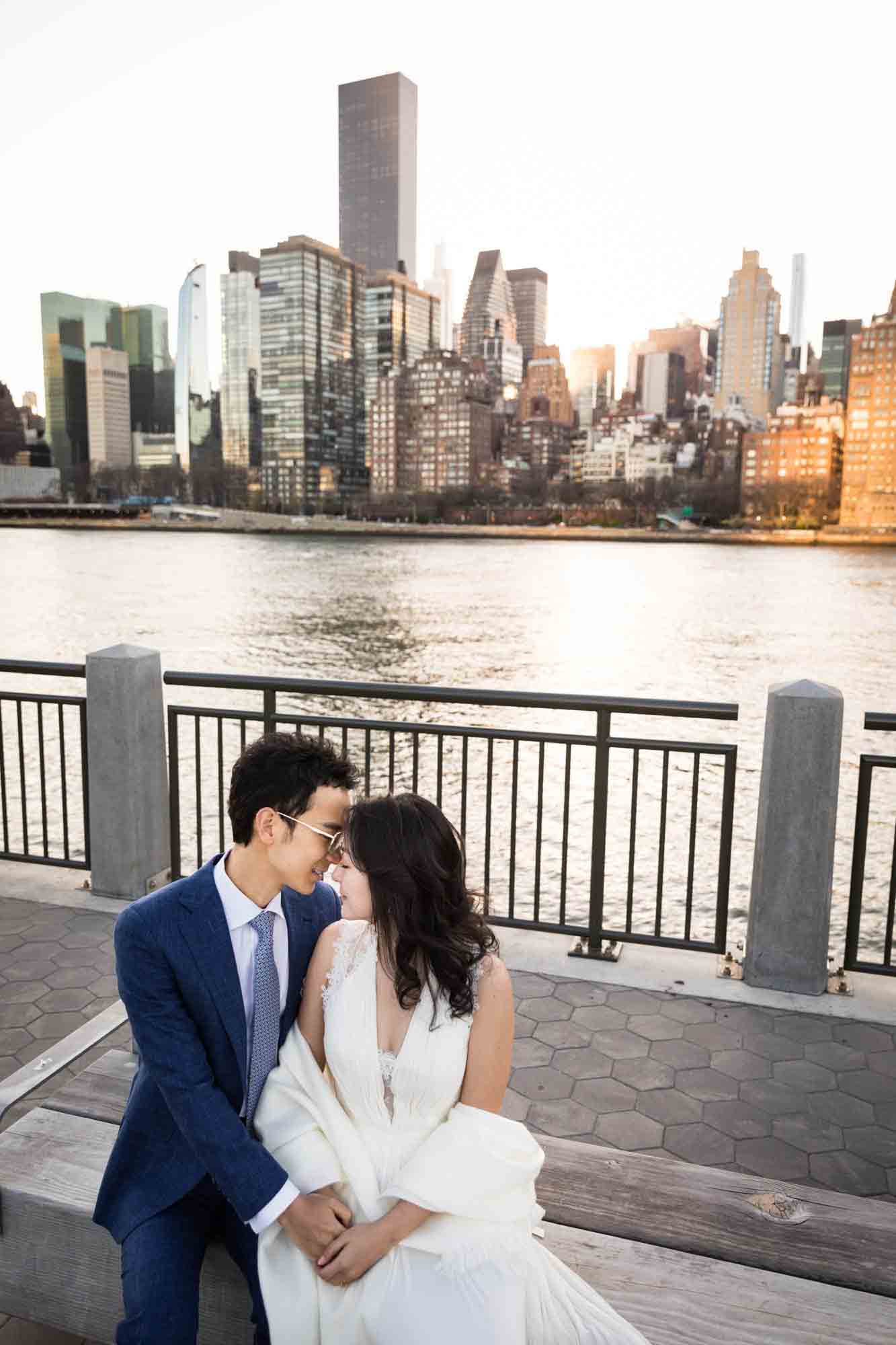 Roosevelt Island engagement photos of couple sitting on bench kissing in front of NYC skyline