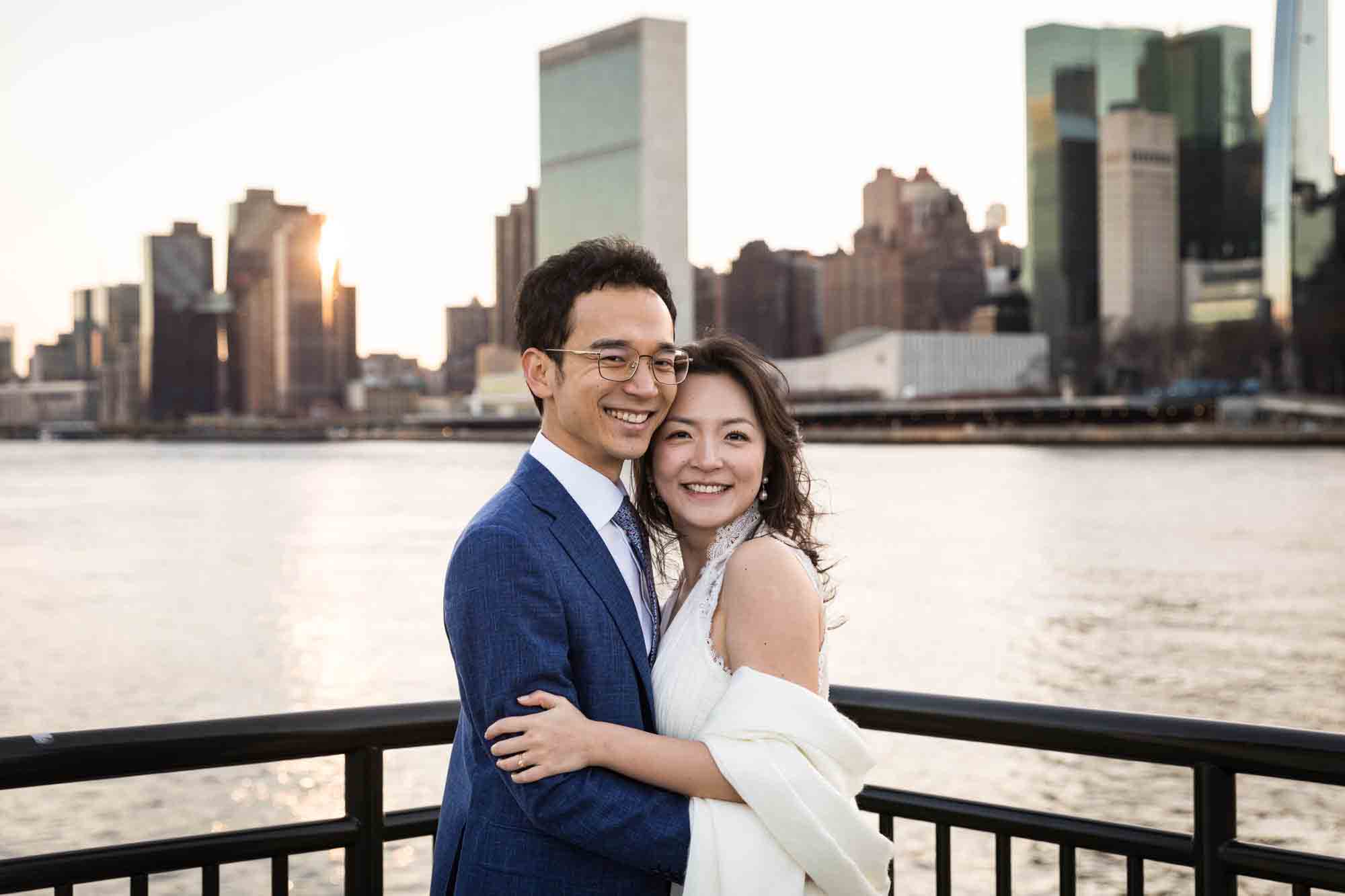 Roosevelt Island engagement photos of couple hugging in front of railing in front of NYC skyline