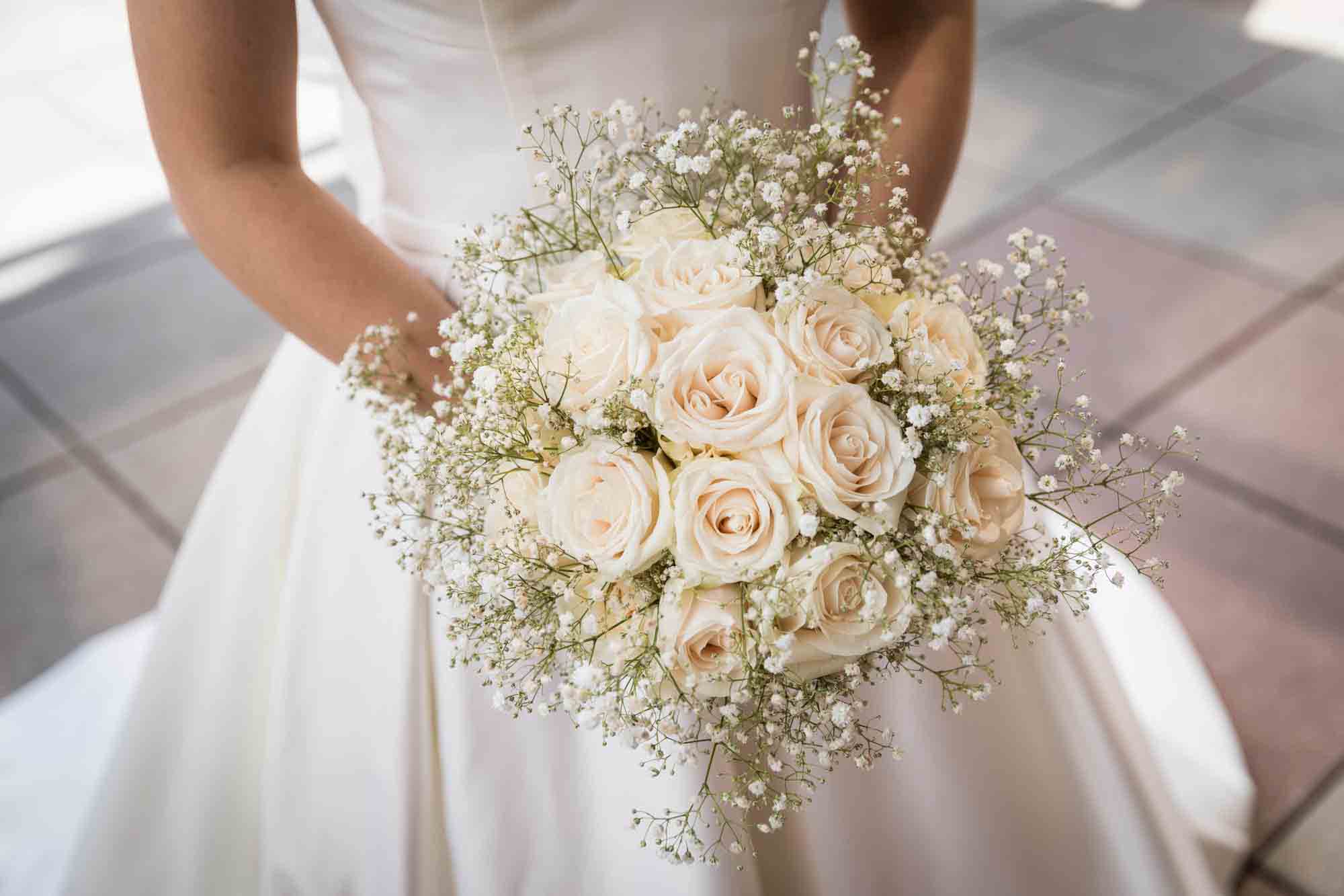 Close up of bride wearing white dress holding flower bouquet of roses and baby's breath at a Sheraton LaGuardia East Hotel wedding