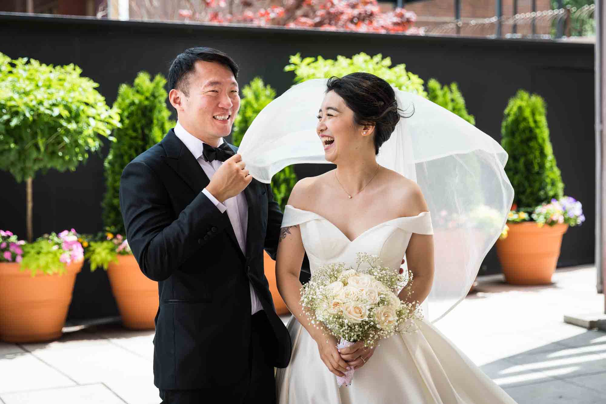 Groom holding laughing bride's veil during portrait session at a Sheraton LaGuardia East Hotel wedding
