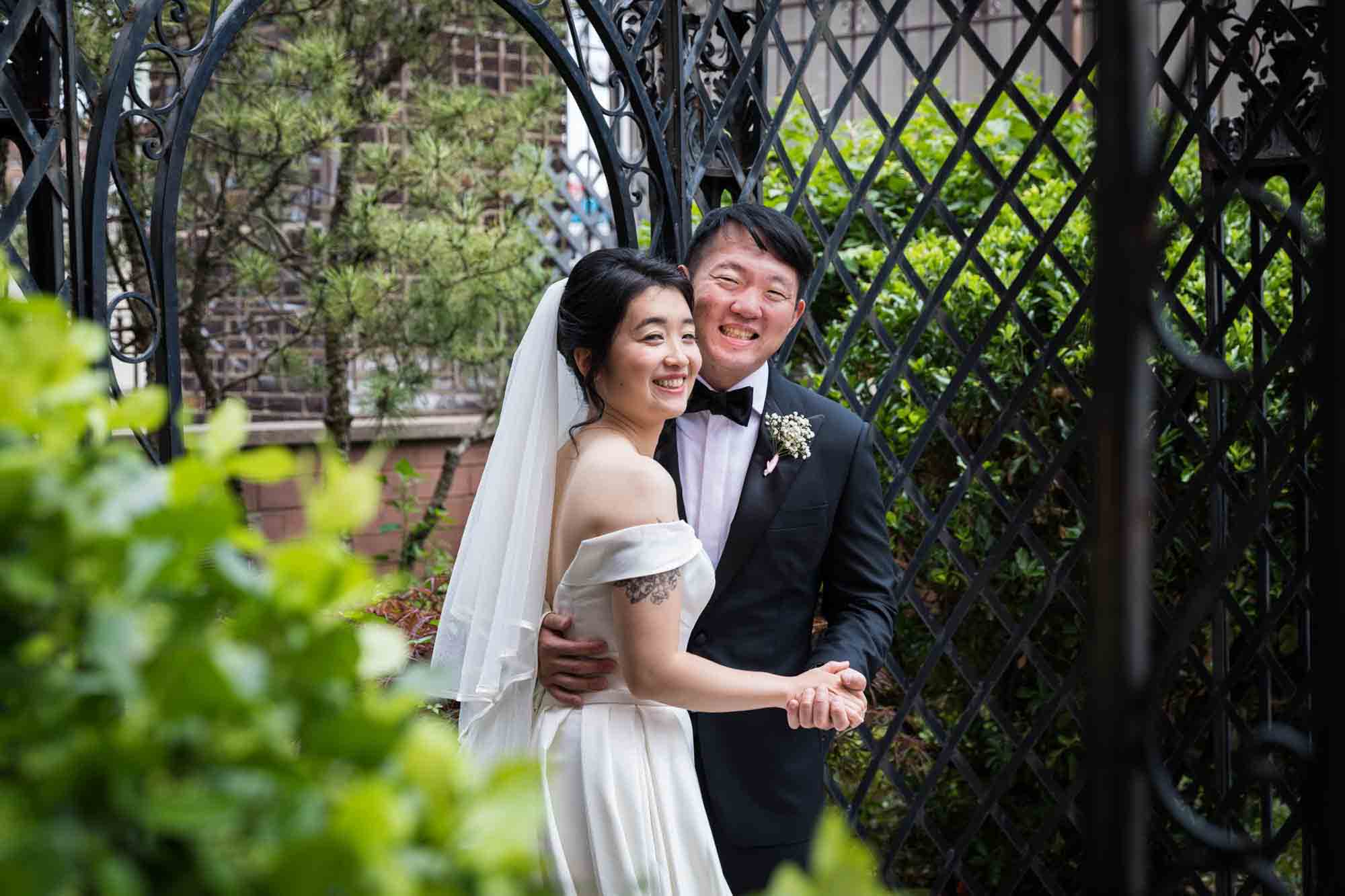 Bride and groom holding hands beside iron latticework gazebo at a Sheraton LaGuardia East Hotel wedding