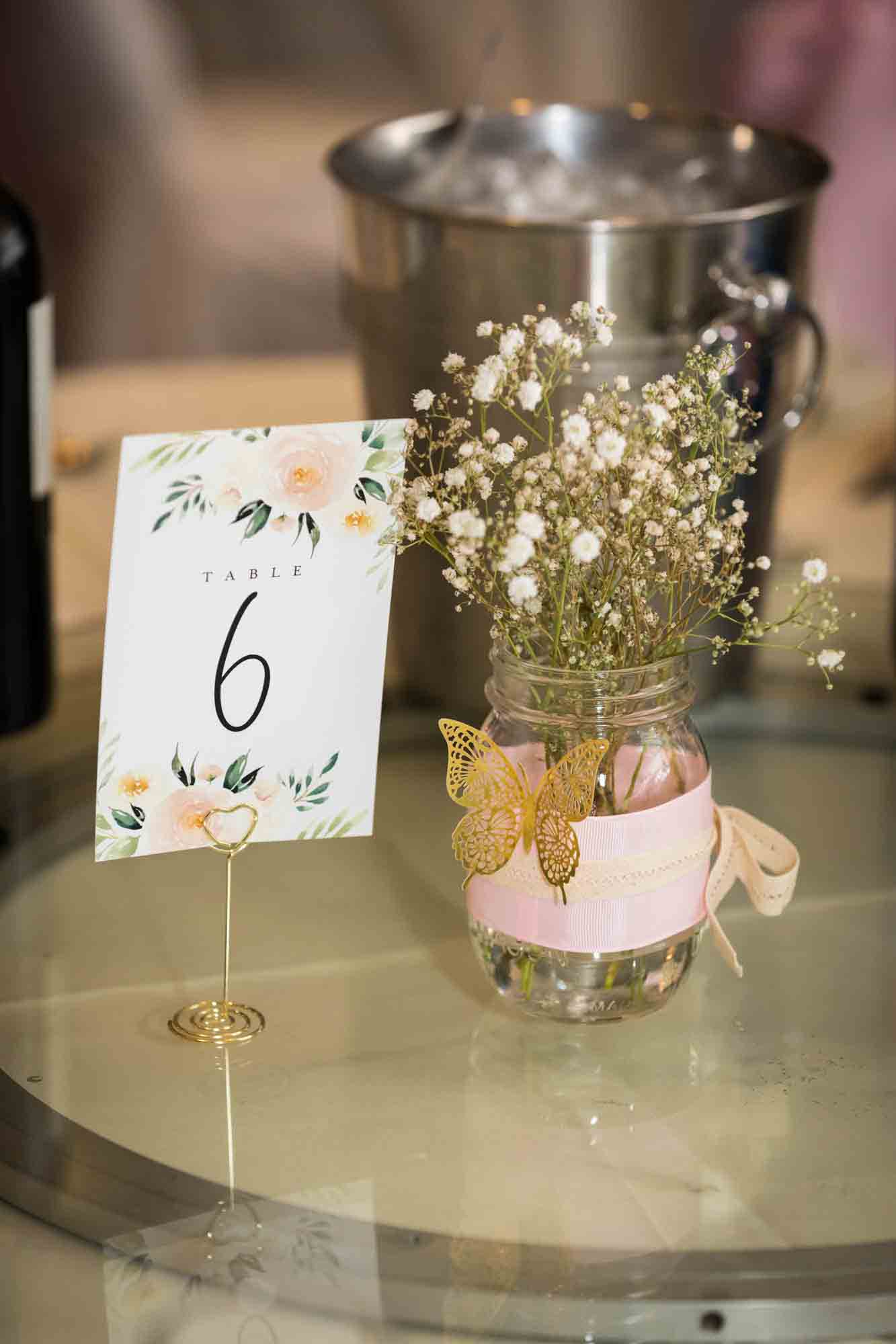 Glass vase holding bouquet of baby's breath with gold butterfly and number 6 table number at a Sheraton LaGuardia East Hotel wedding
