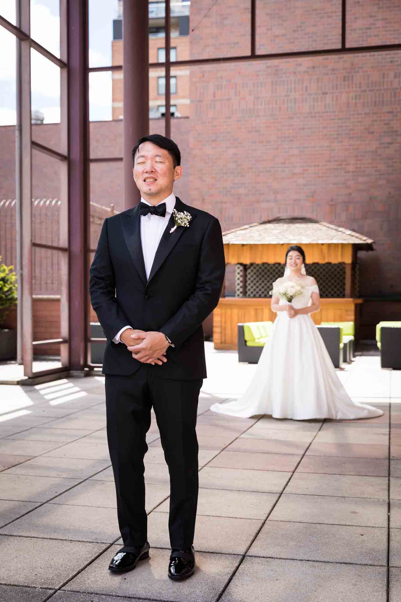 Groom standing with eyes closed waiting for bride behind him during first look at a Sheraton LaGuardia East Hotel wedding