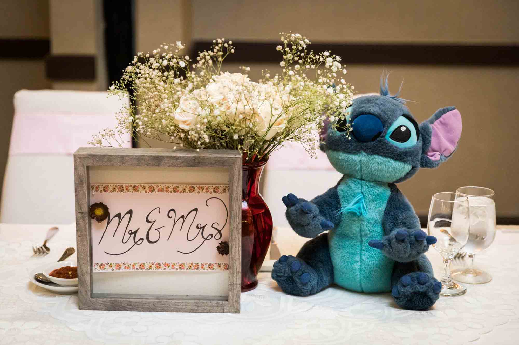 Sweetheart table centerpiece with 'Mr. and Mrs.' sign, flower bouquet, and stuffed blue animal at a Sheraton LaGuardia East Hotel wedding