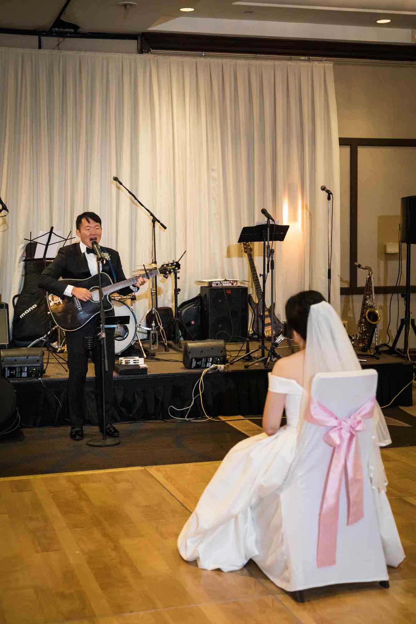 Groom performing with guitar singing to bride sitting in chair at a Sheraton LaGuardia East Hotel wedding