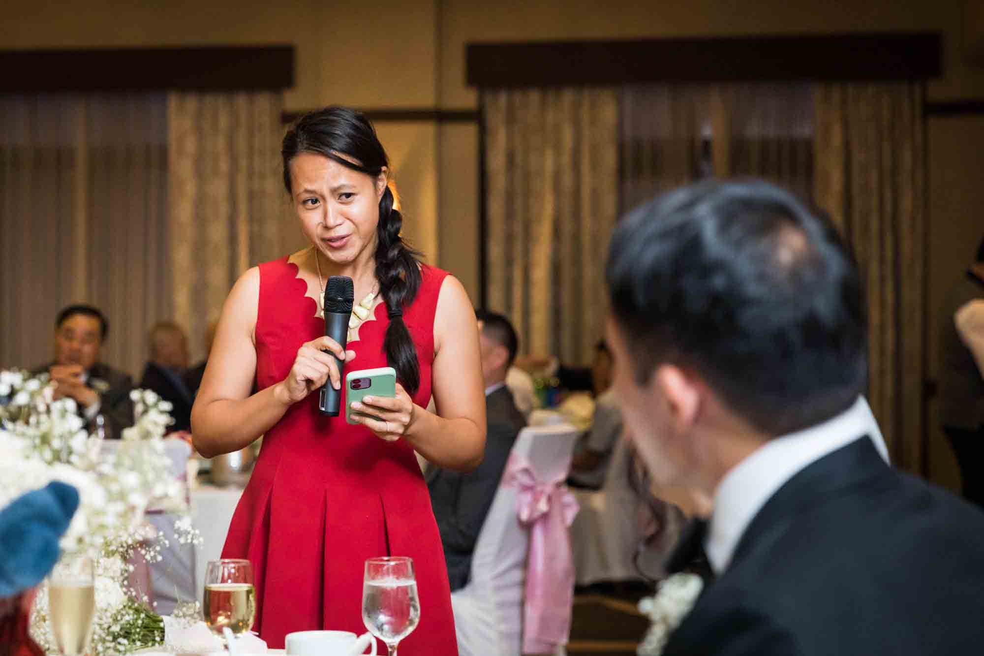 Woman wearing red dress talking into microphone in front of bride and groom at a Sheraton LaGuardia East Hotel wedding
