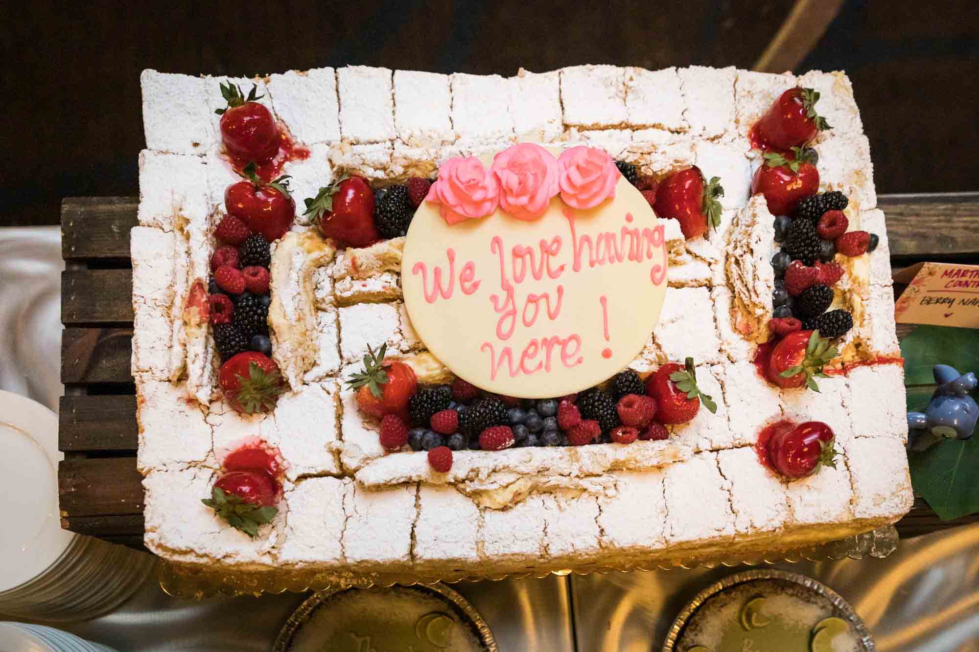 White cake decorated with strawberries and frosting reading 'We love having you here' at a Sheraton LaGuardia East Hotel wedding