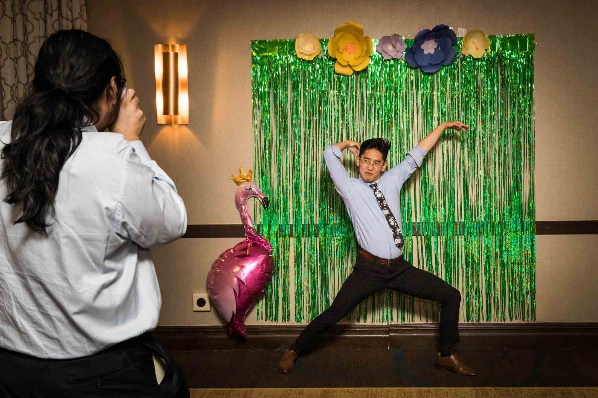 Woman photographing man making funny pose in front of photobooth at a Sheraton LaGuardia East Hotel wedding