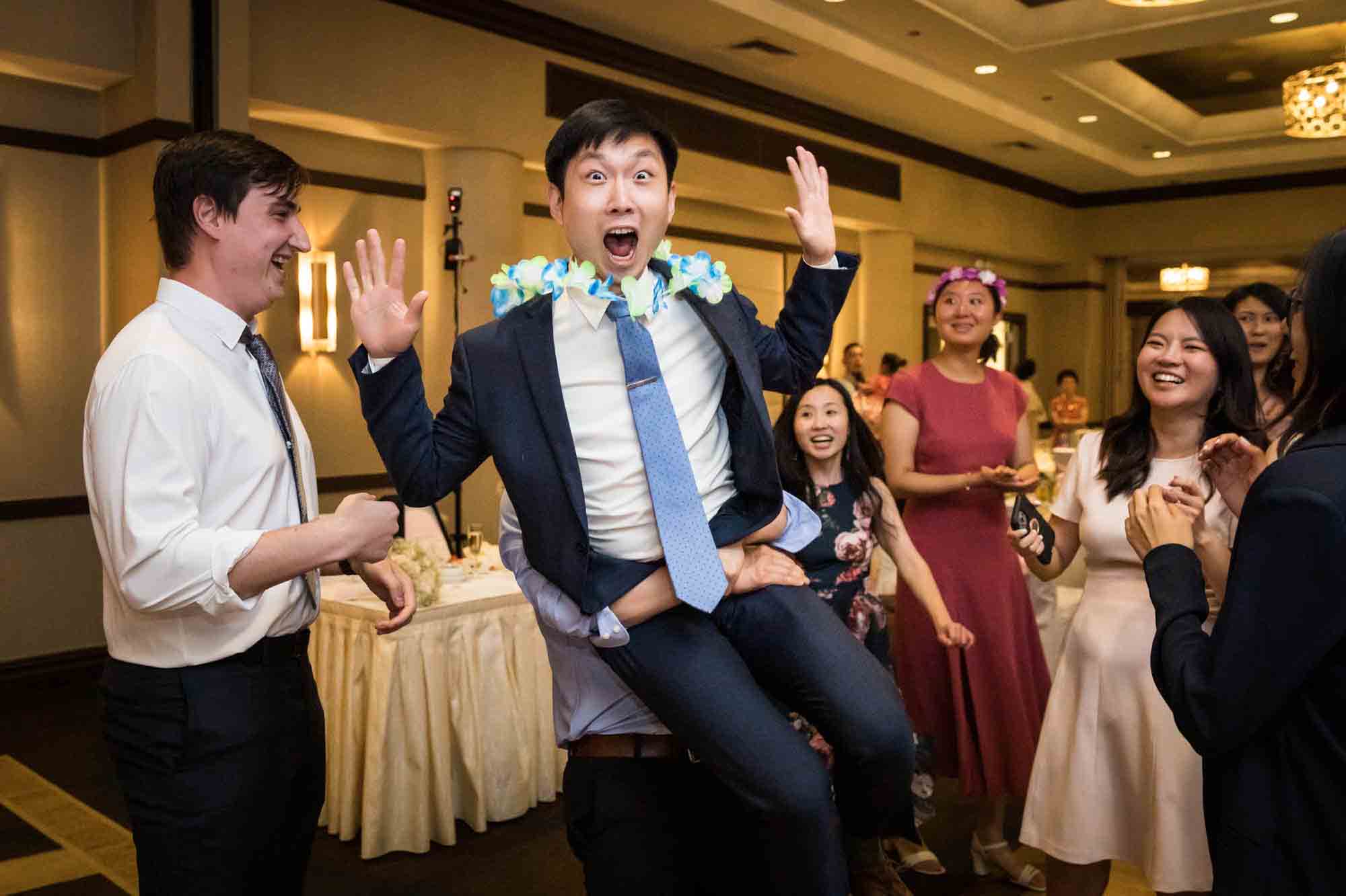 Male guest making funny face while being lifted in the air at a Sheraton LaGuardia East Hotel wedding