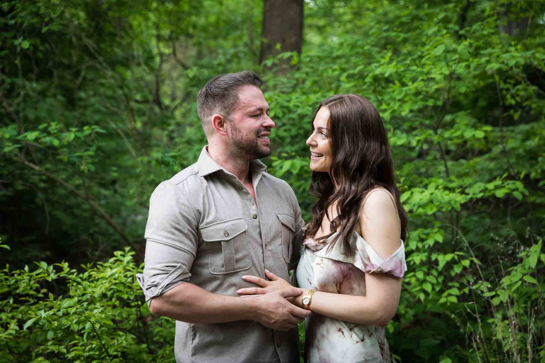 Couple hugging in front of trees and leaves Woman looking at engagement ring on finger during a Central Park surprise proposal