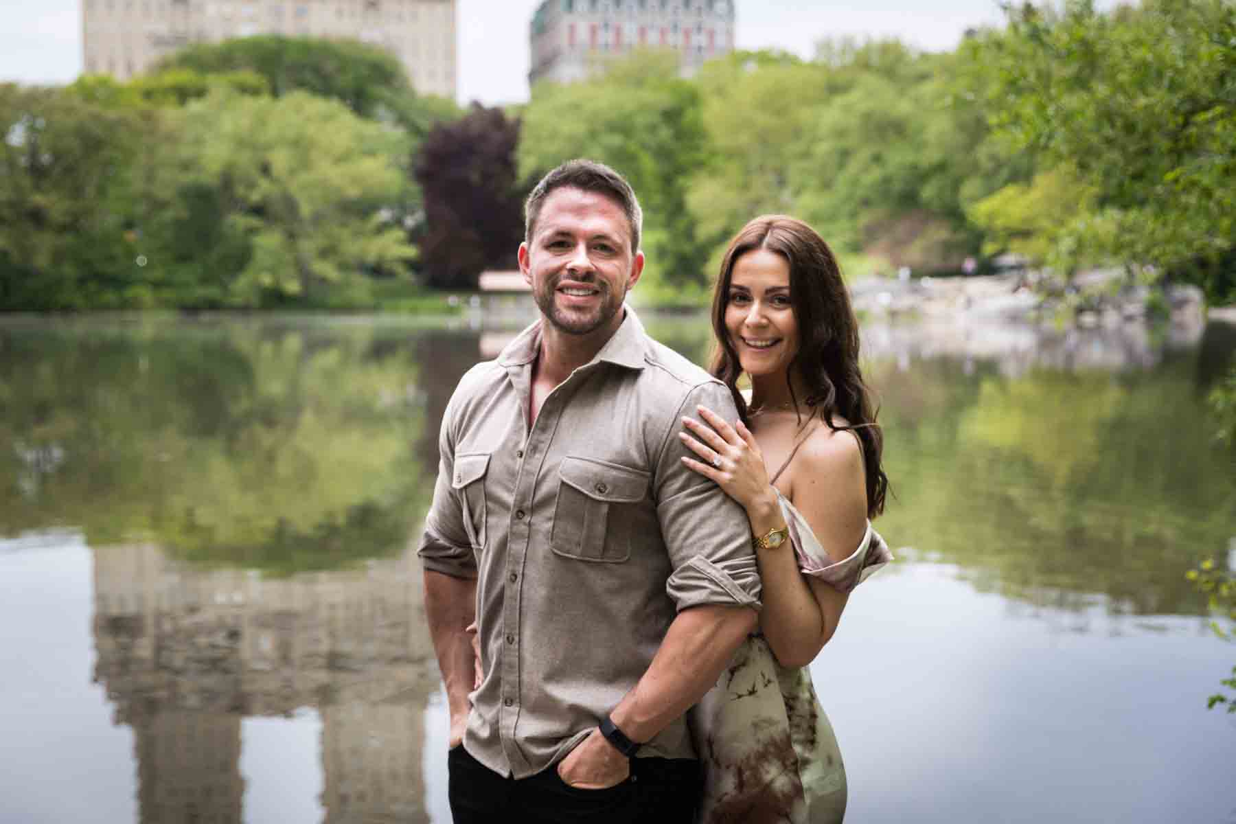 Couple standing in front of lake with buildings reflected in water for an article on the best places to propose in Central Park