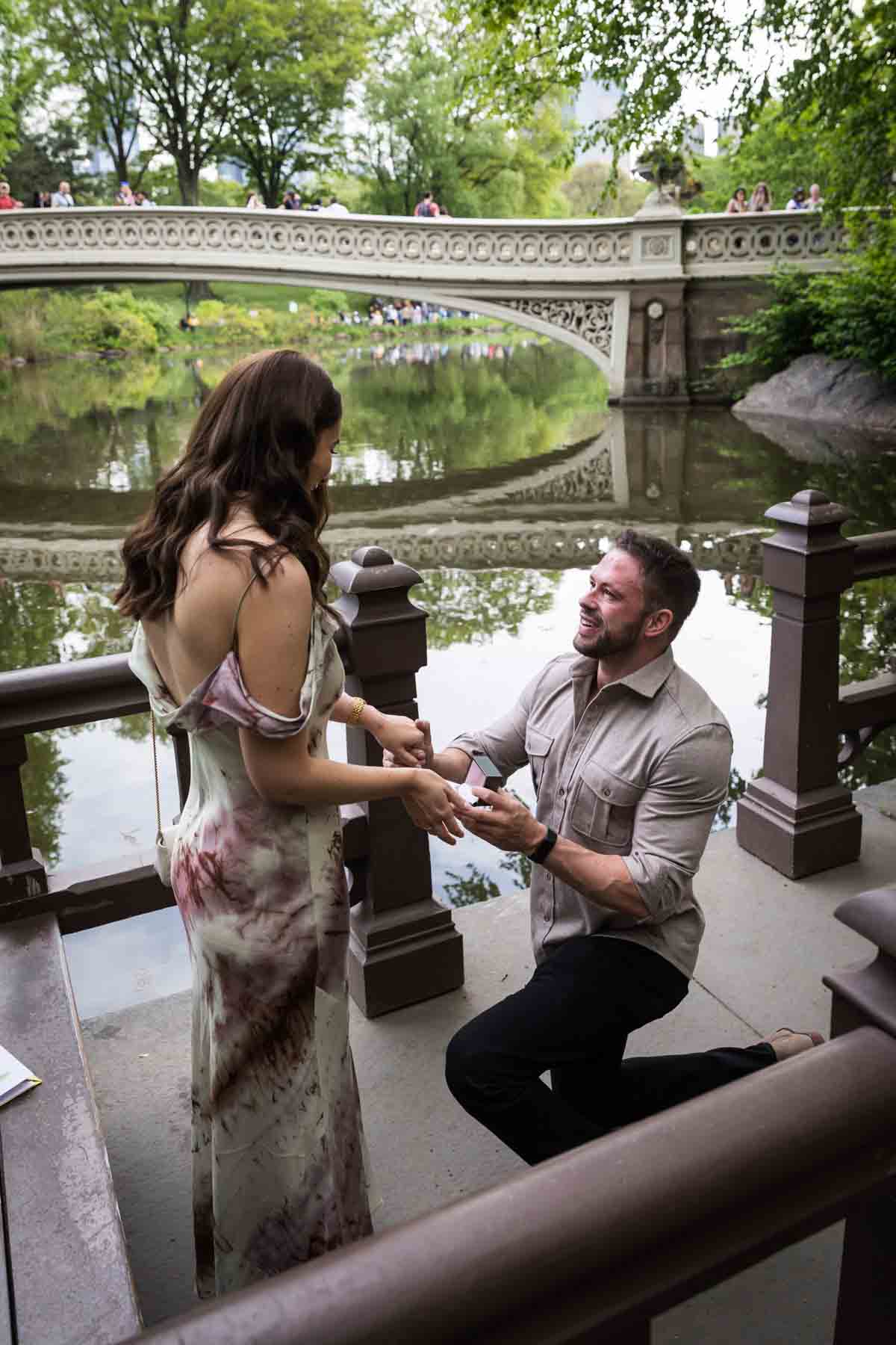 Man down on one knee asking girl to marry him on dock during a Central Park surprise proposal