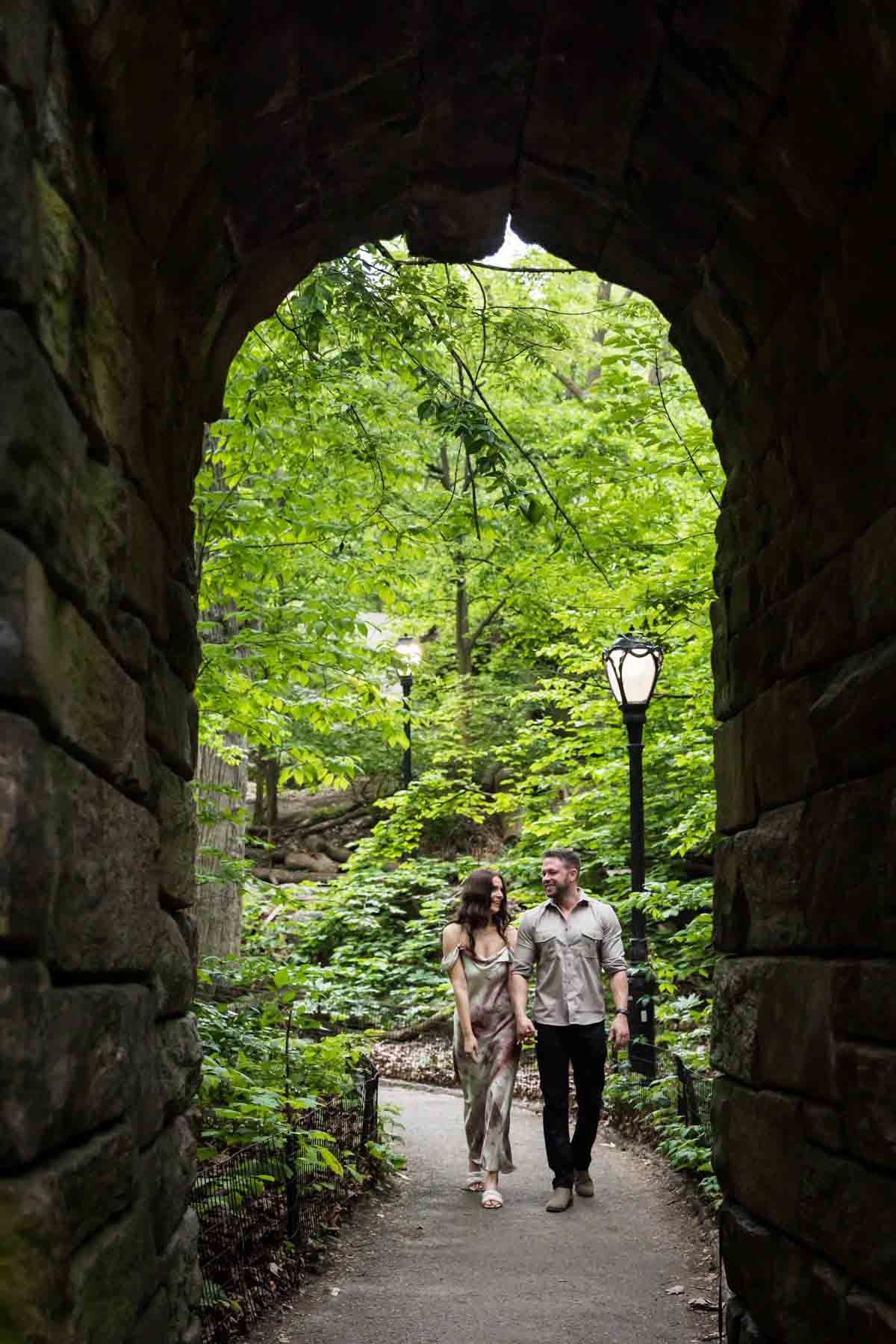 View through stone arch of couple walking in park during a Central Park surprise proposal