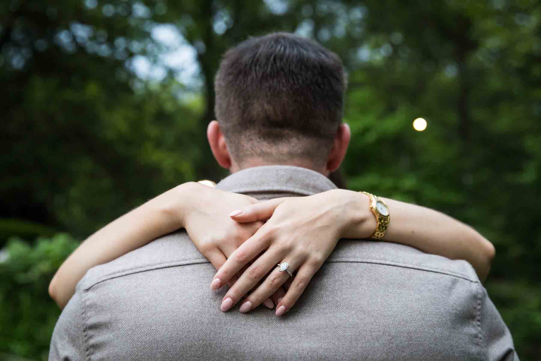 Close up of woman's hands wearing engagement ring around man's neck