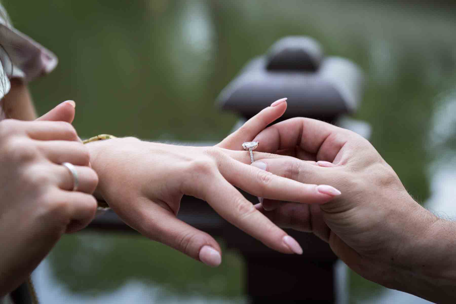 Close up of man putting engagement ring on woman's finger for an article on the best places to propose in Central Park 