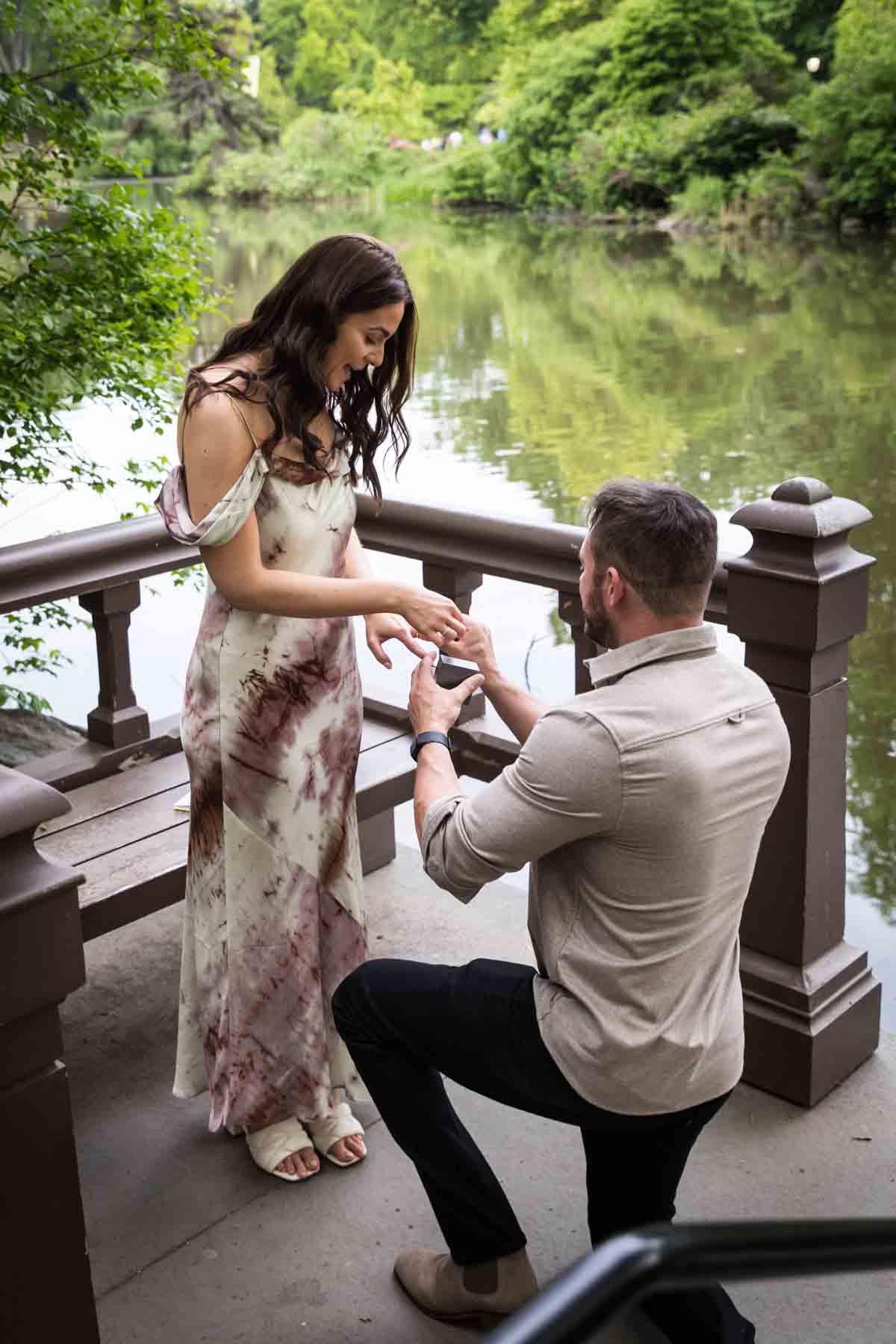 Man down on one knee asking girl to marry him on dock during a Central Park surprise proposal